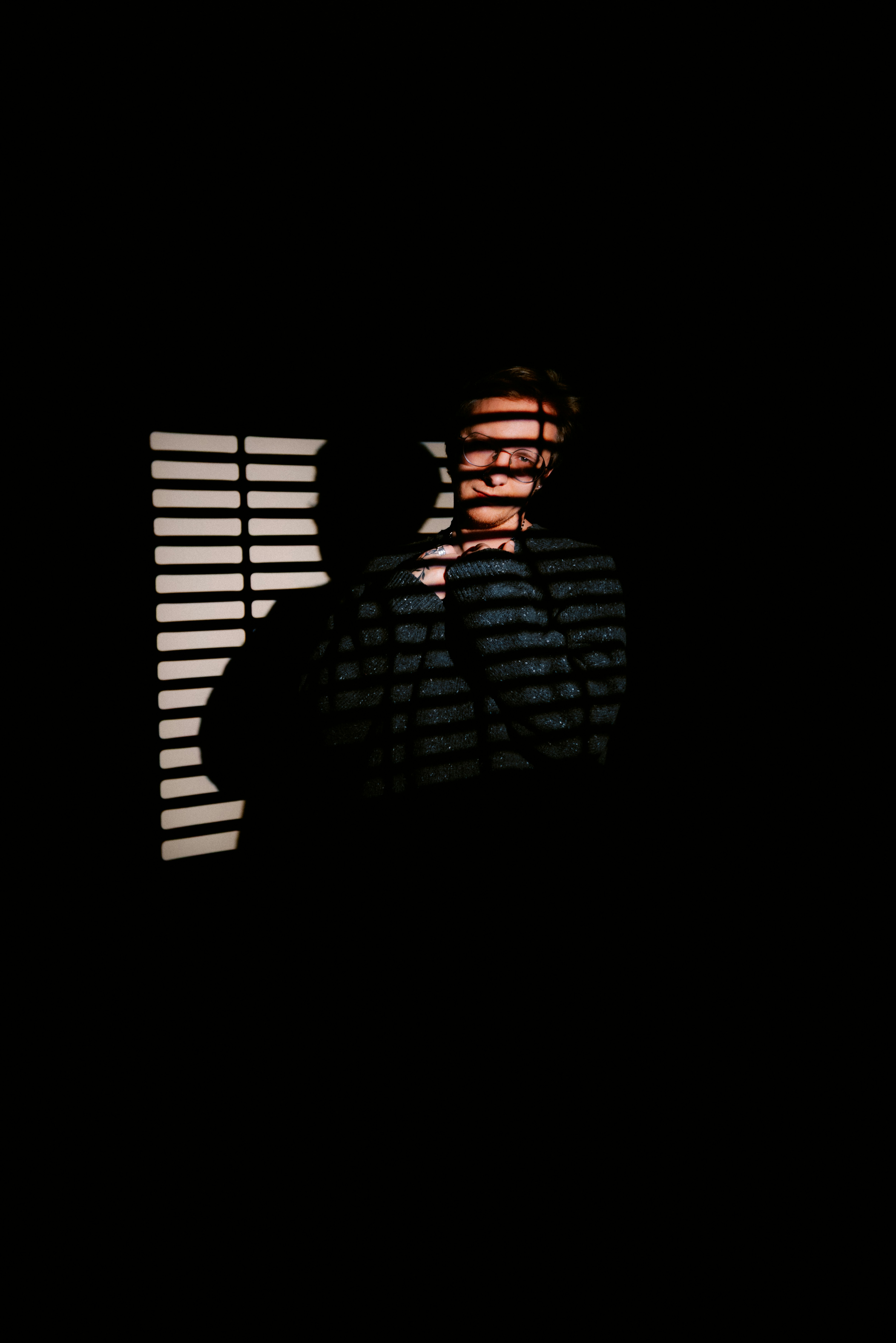 Man in shadows with blinds casting striped light.