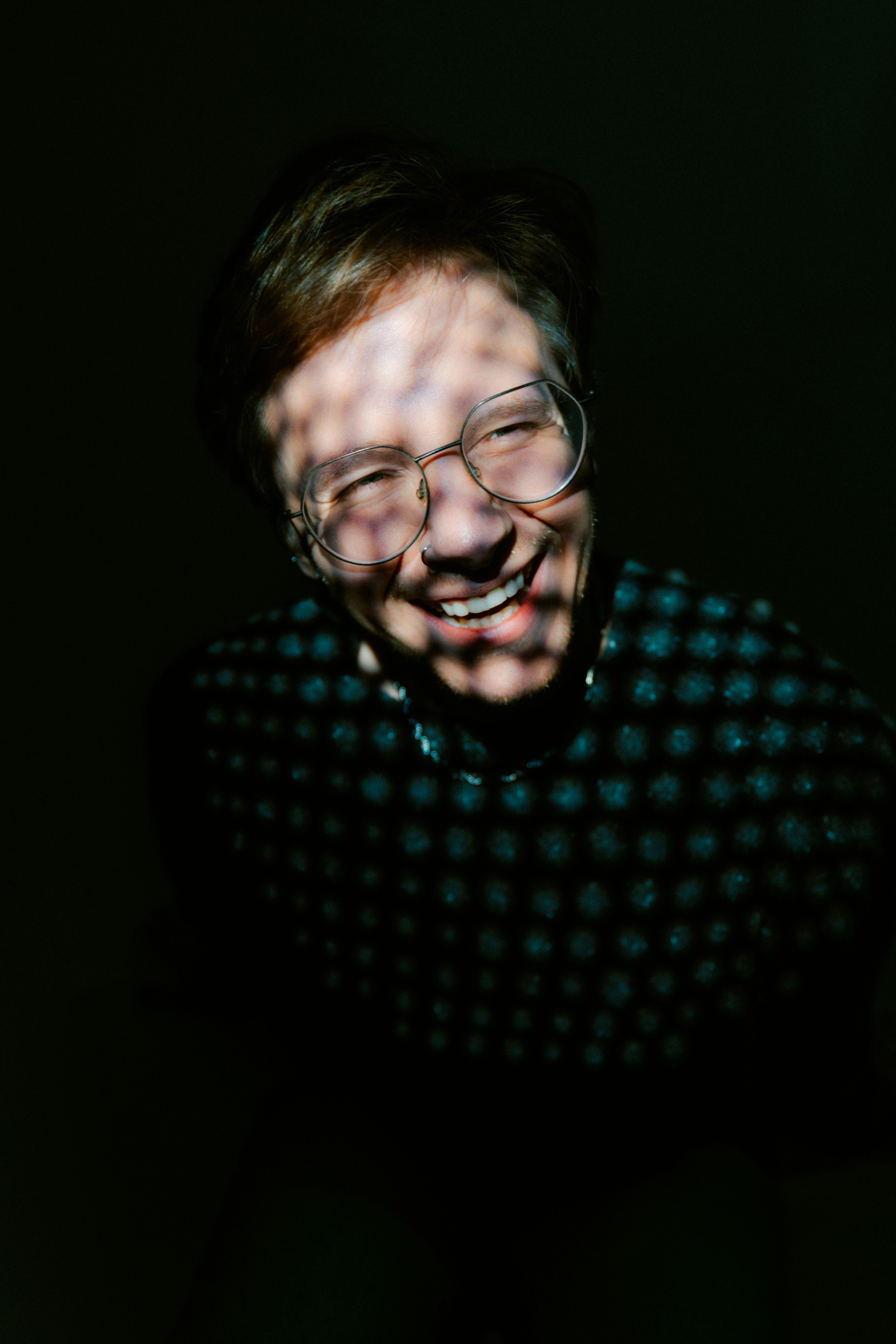 A person with glasses smiles, lit by patterned light