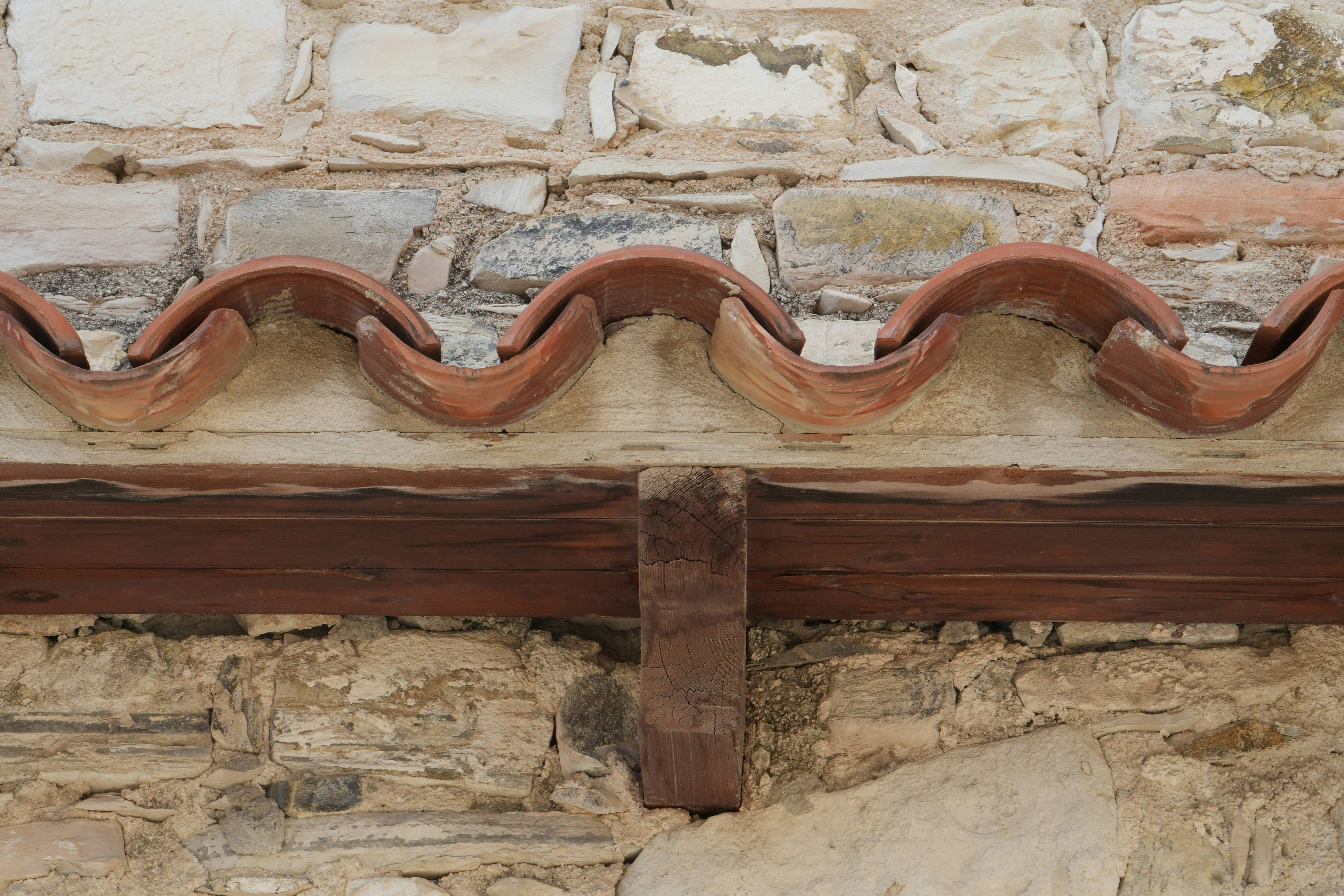 Close-up of ancient stone wall with terracotta roof tiles.