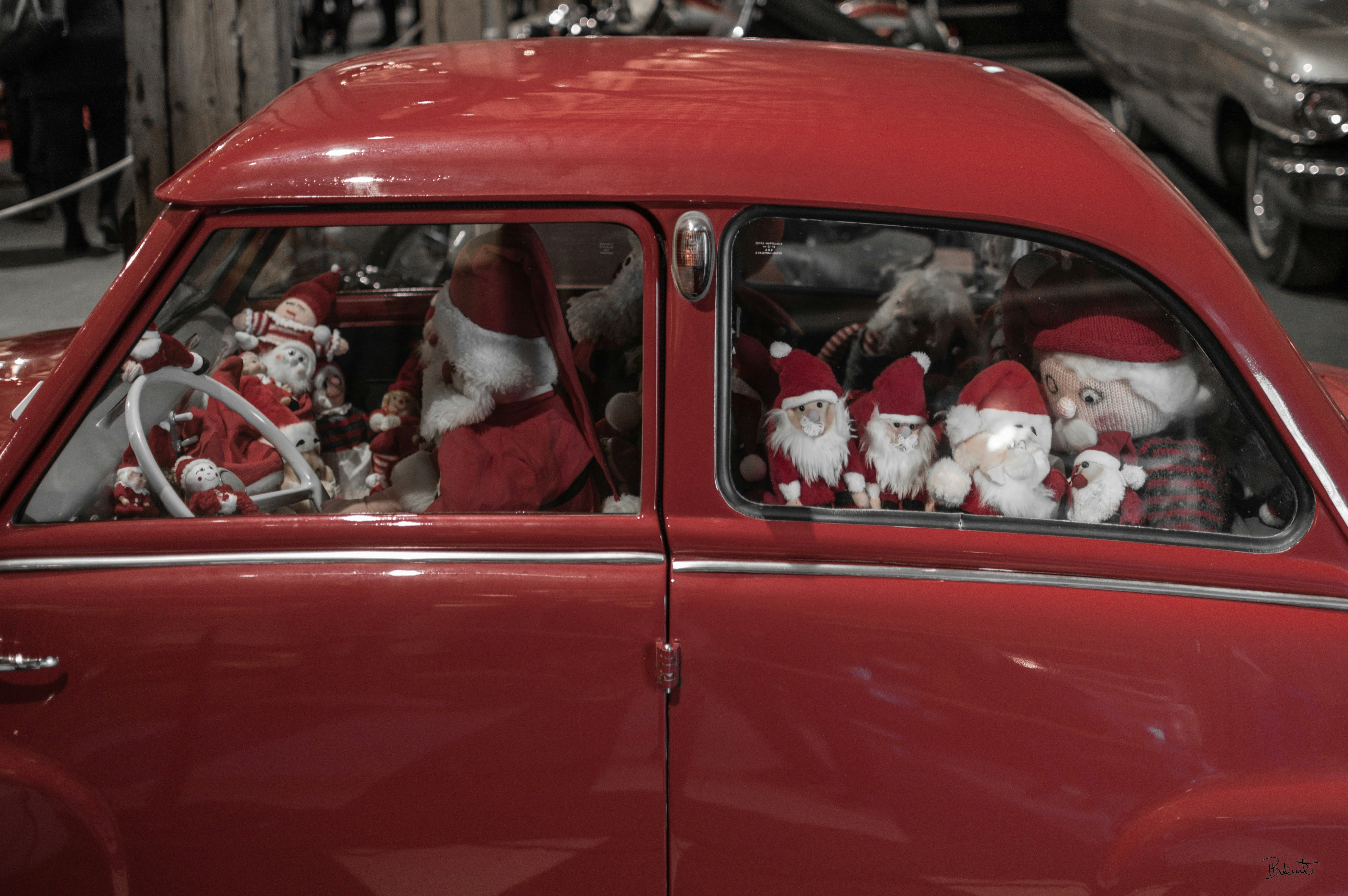 Several santa claus dolls inside a red car.