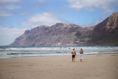 Two people walk on a sandy beach towards the ocean.