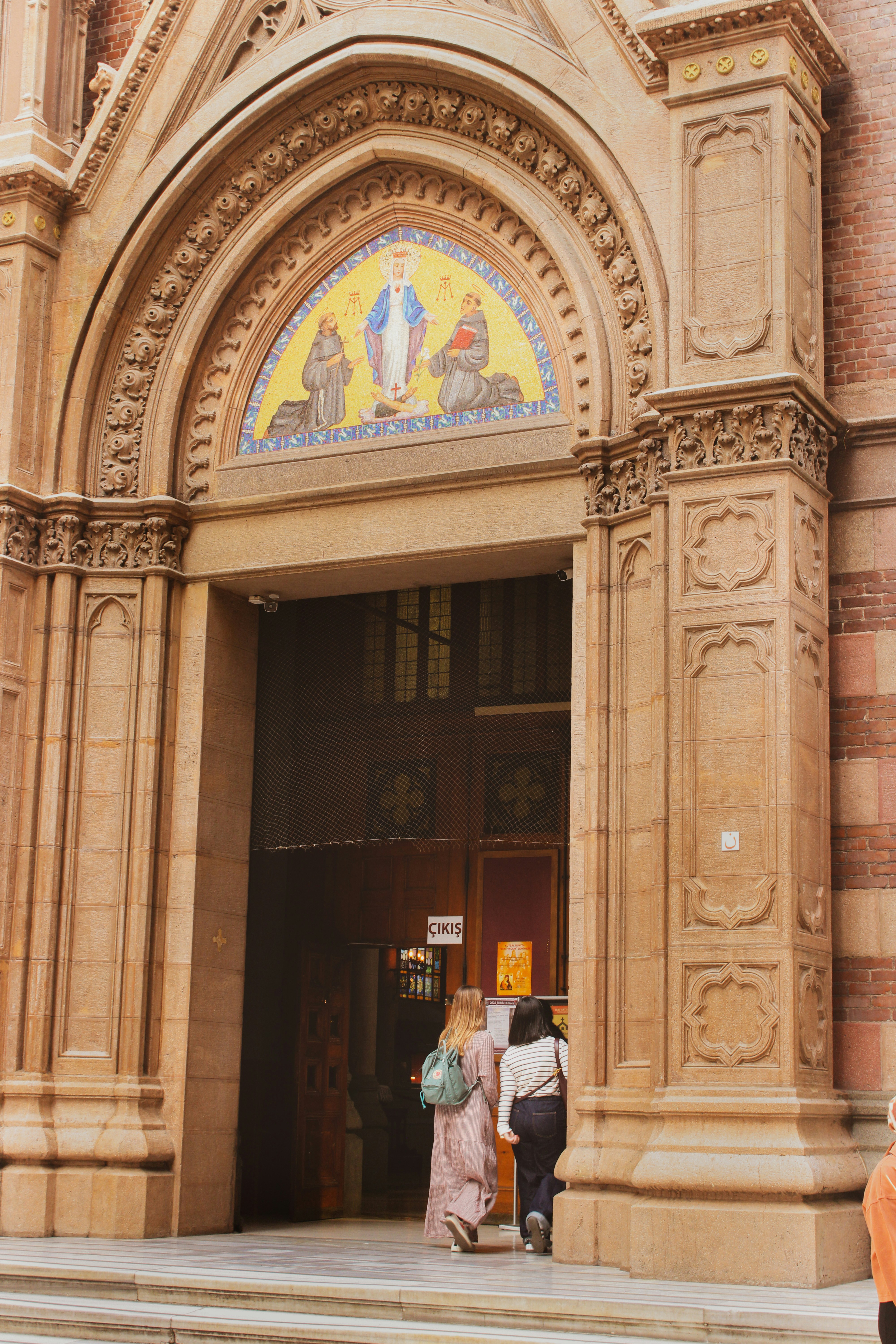 Personas entrando a una iglesia ornamentada con mosaico sobre la entrada