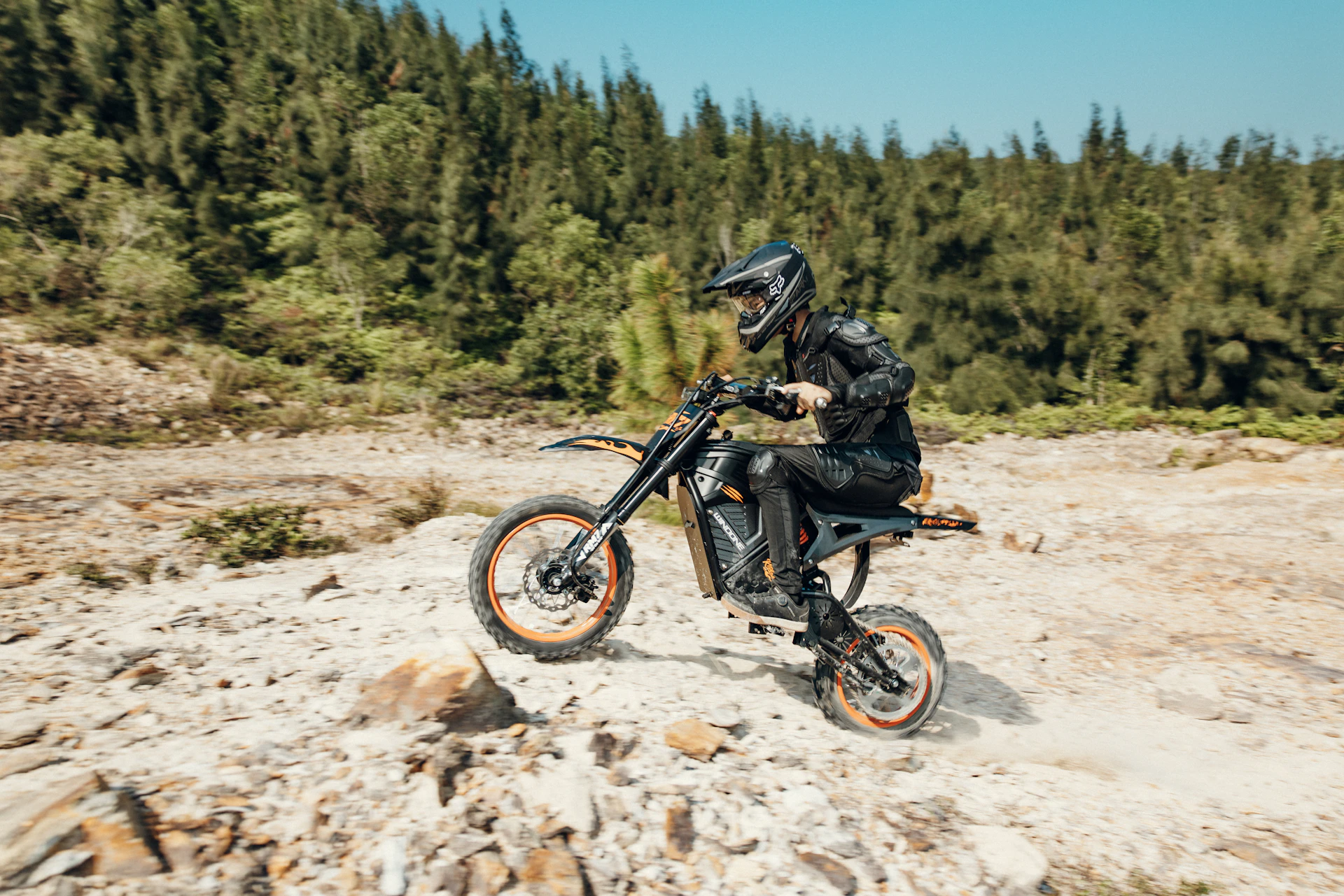 Rider on dirt bike navigating rocky terrain with trees.