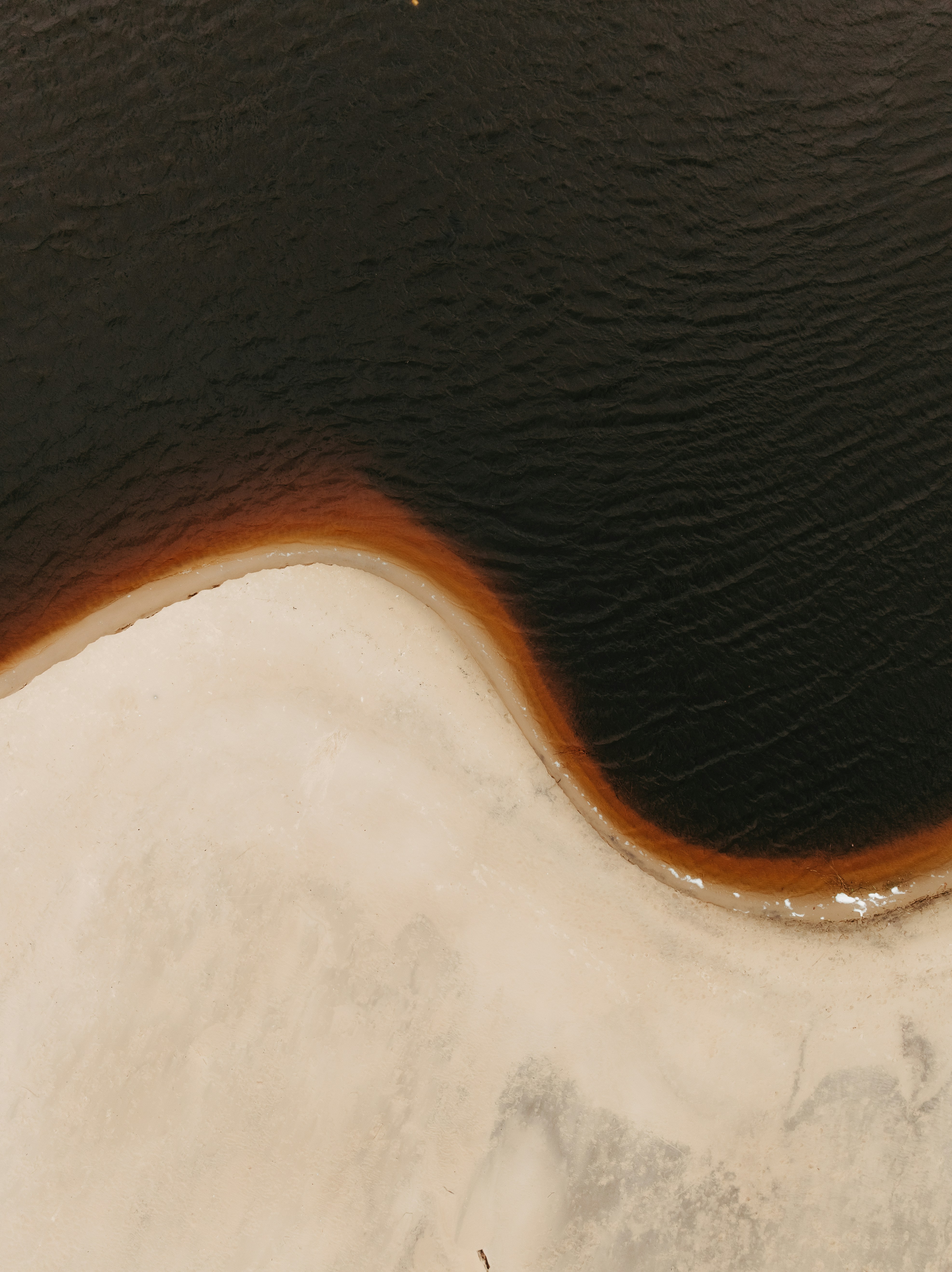 Dark water meets sandy shore with reddish brown edge