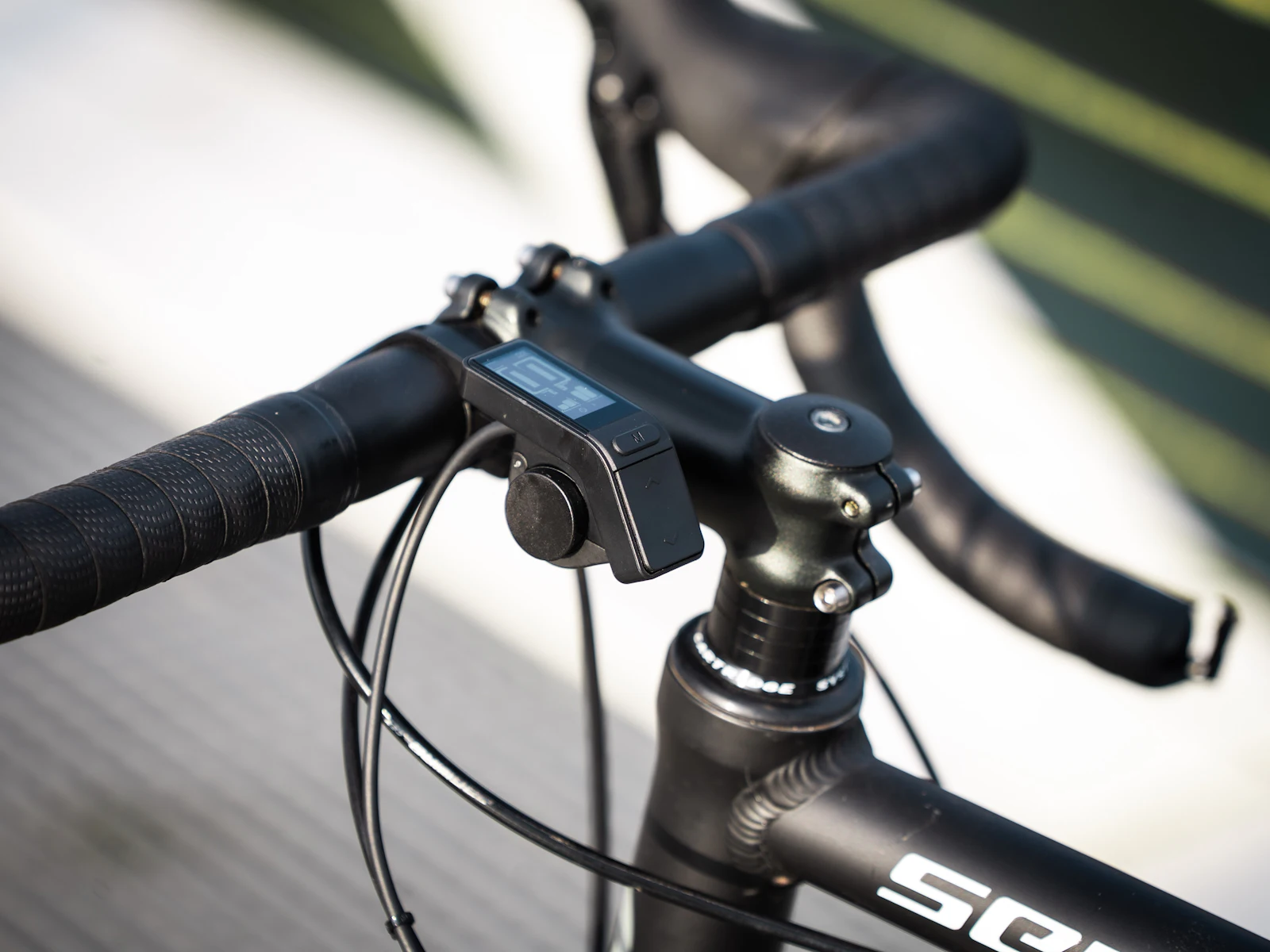 Close-up of a black road bike handlebar with a small cycling computer mounted on the stem