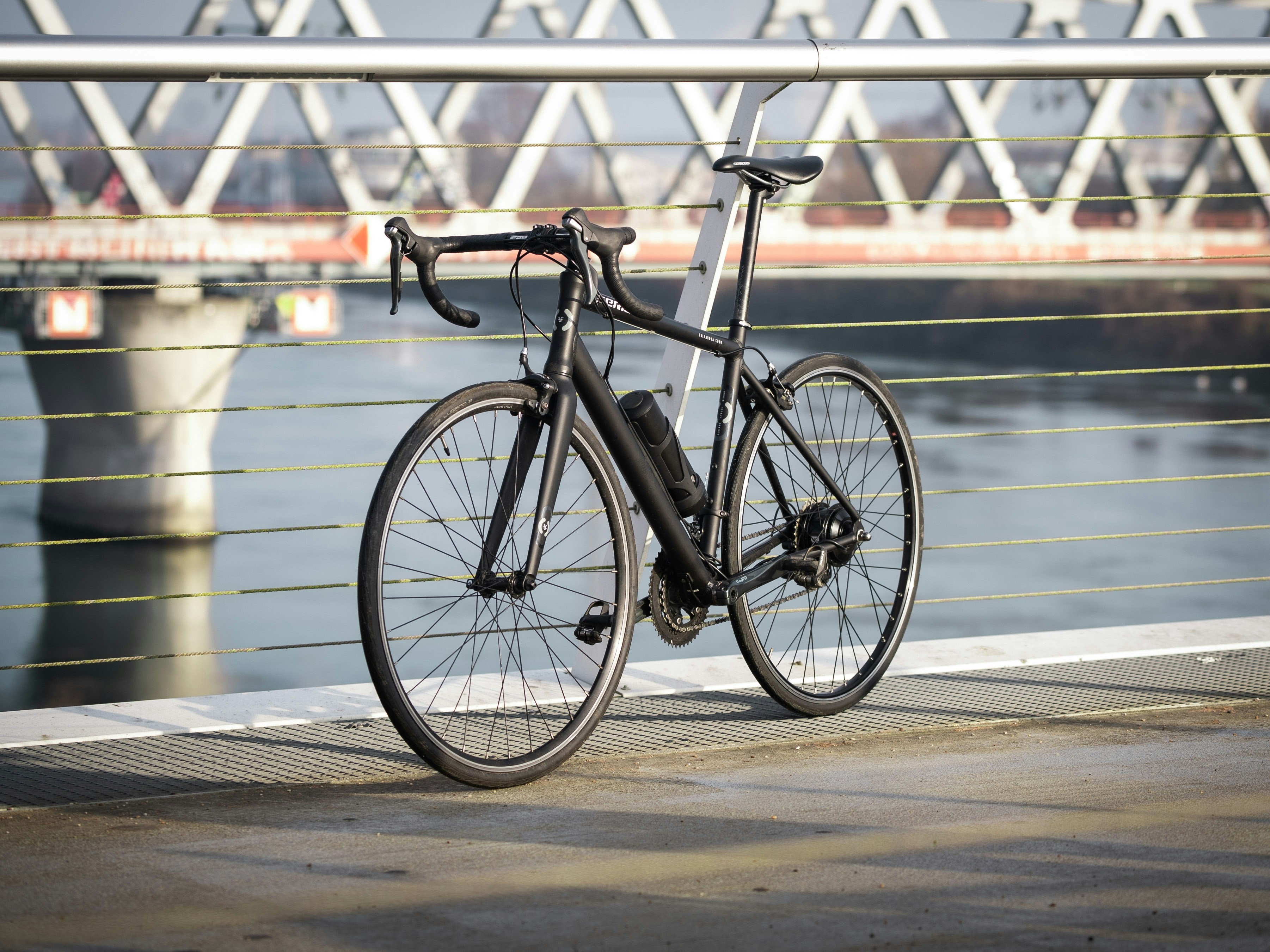 A black road bicycle parked outdoors by a railing.