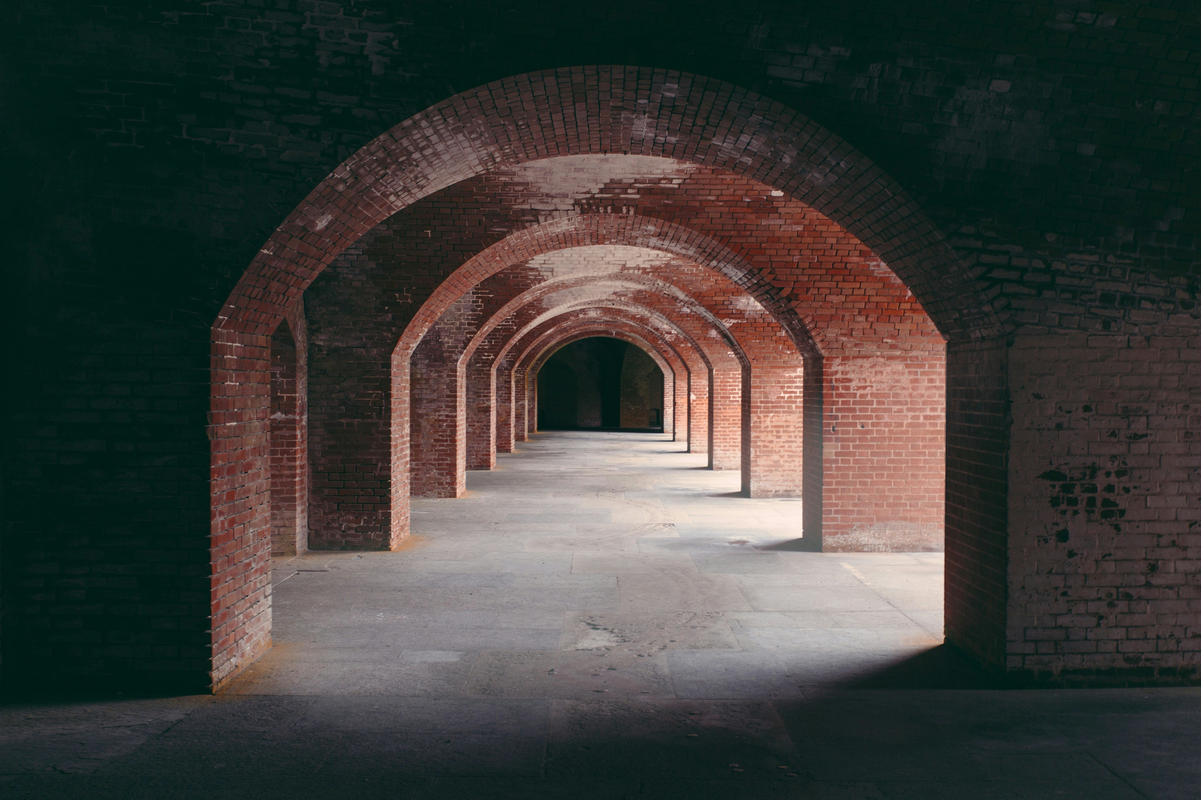 A series of red brick arches forming a long corridor with stone flooring