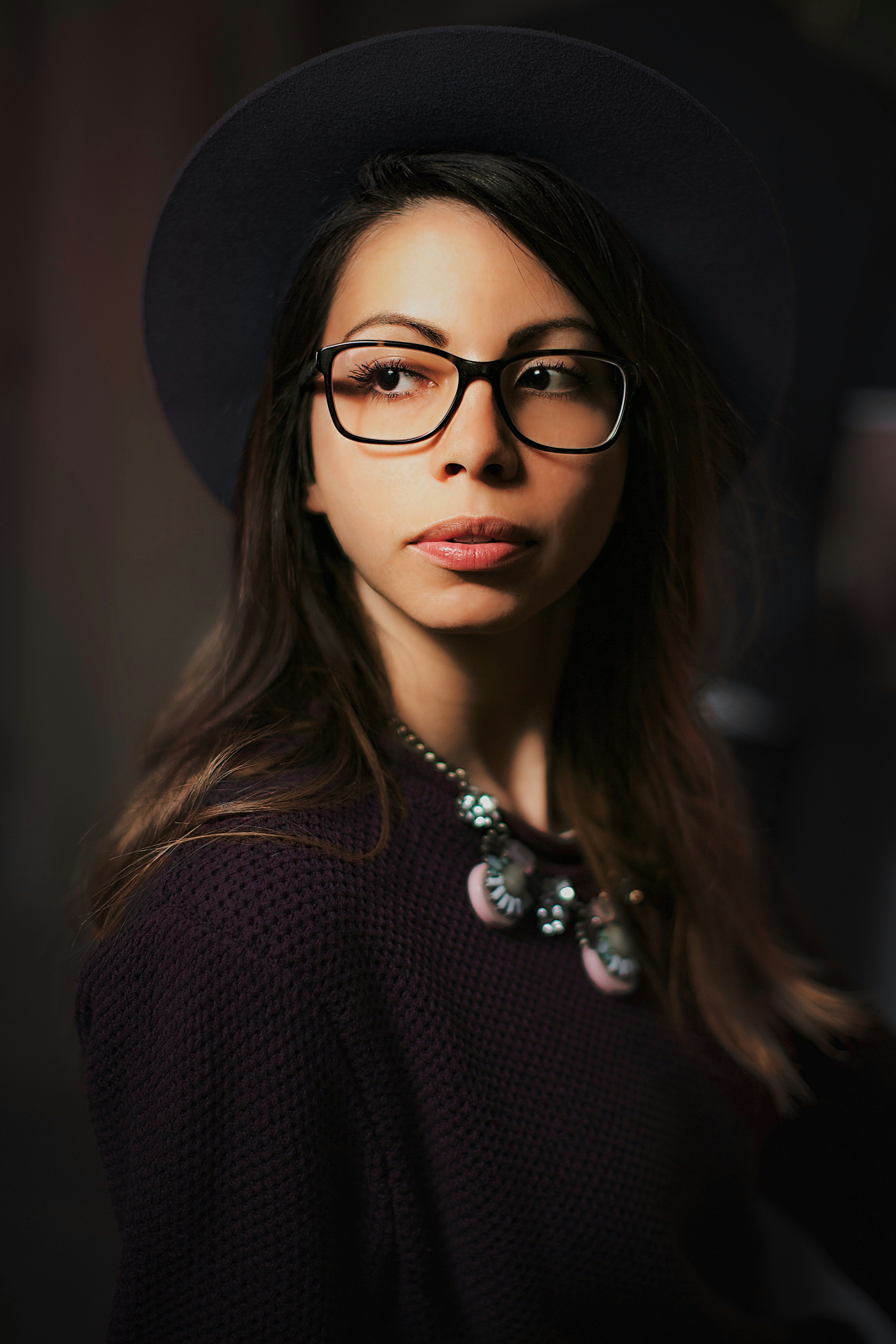 A woman wearing a dark hat, glasses, and a statement necklace