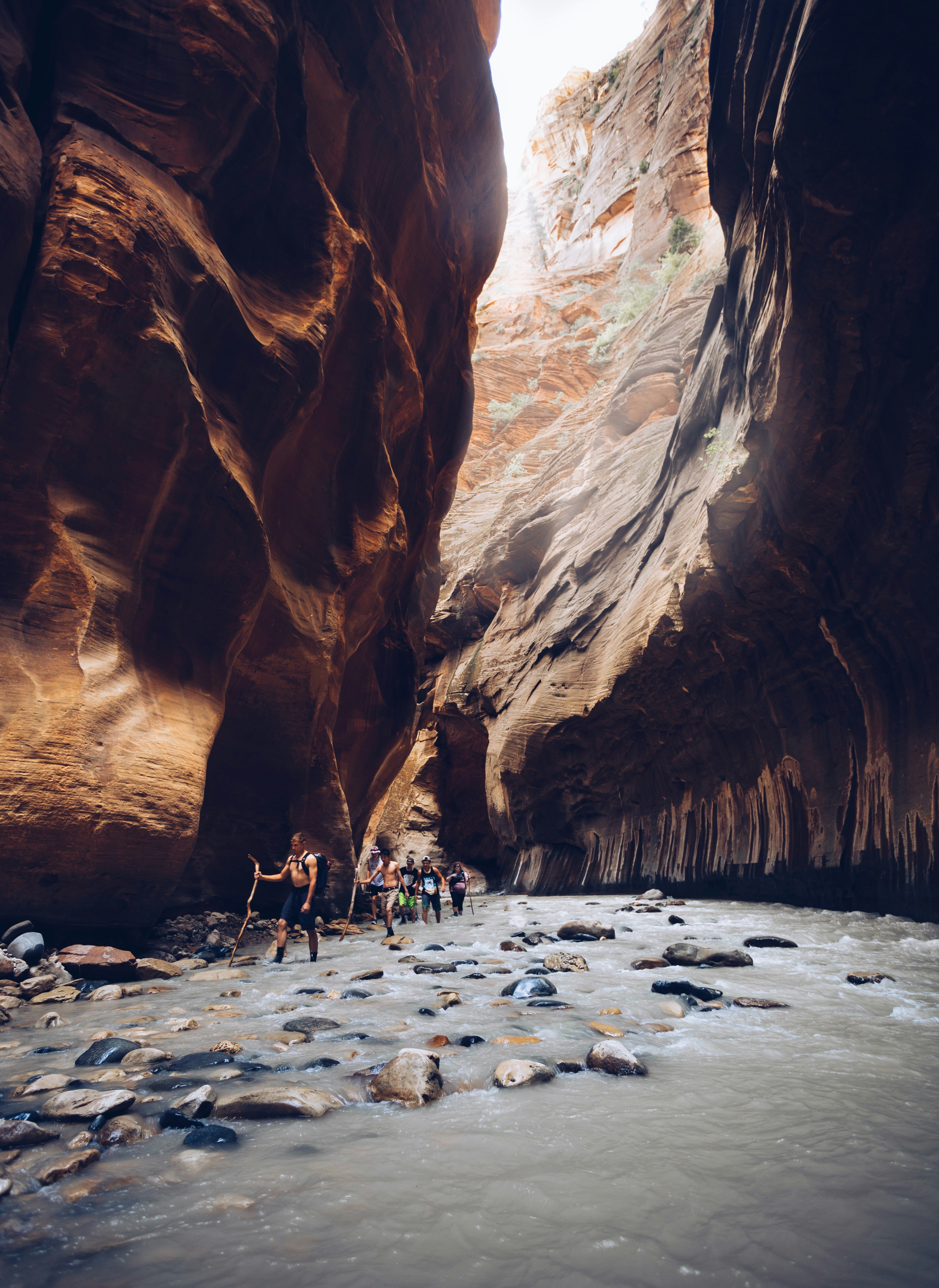 A group of people hiking through a narrow river canyon with tall sandstone walls