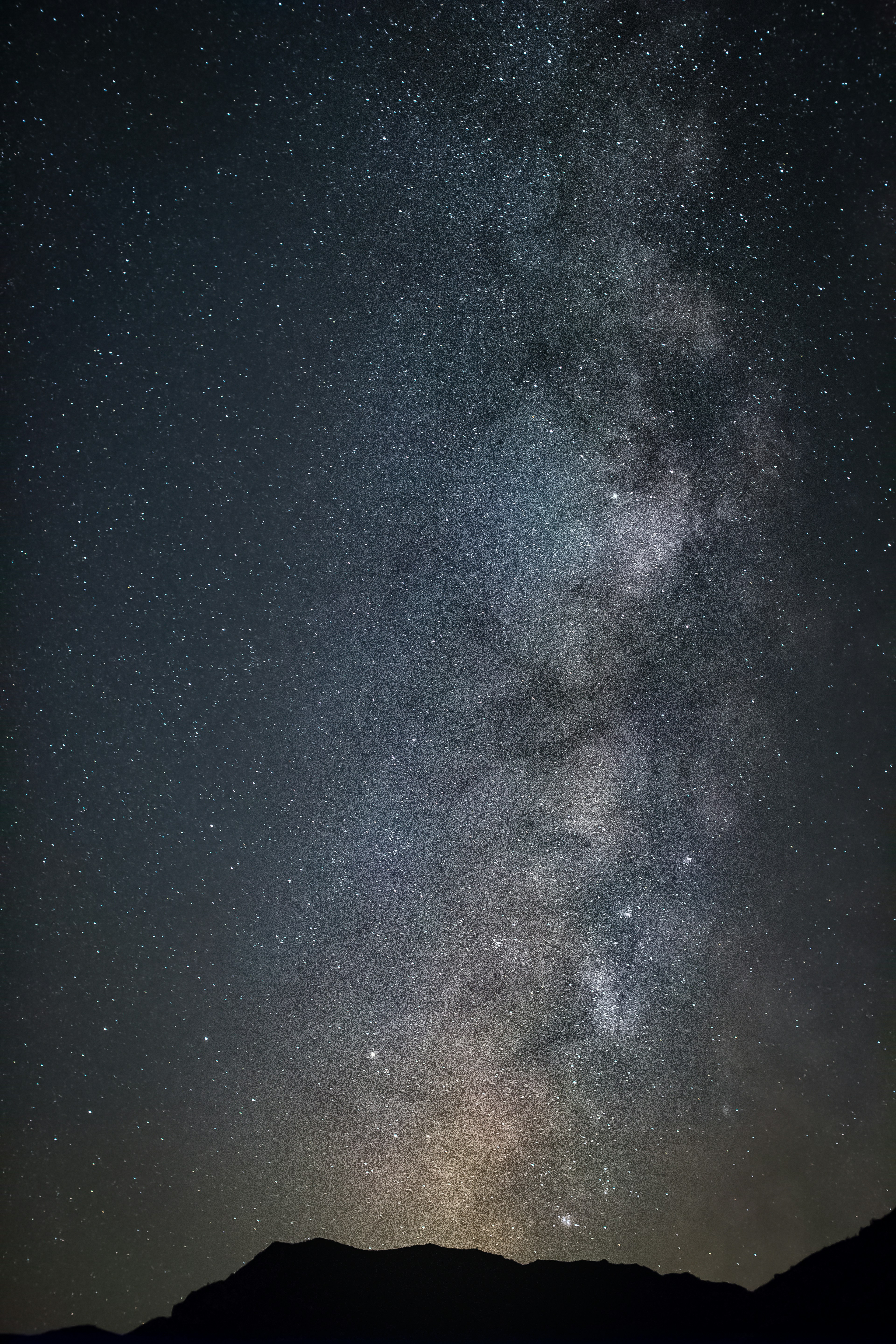 The Milky Way galaxy stretching across a dark night sky above a mountain silhouette
