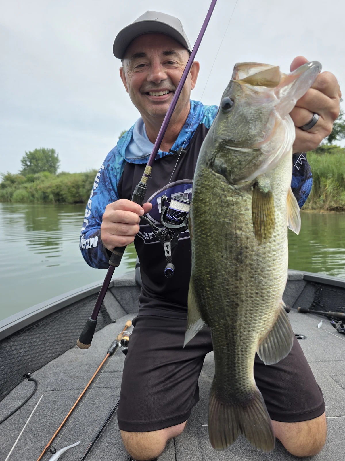 A grinning angler in a cap holds up a big fish on his boat