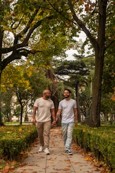 A gay couple holding hands walking in a park.