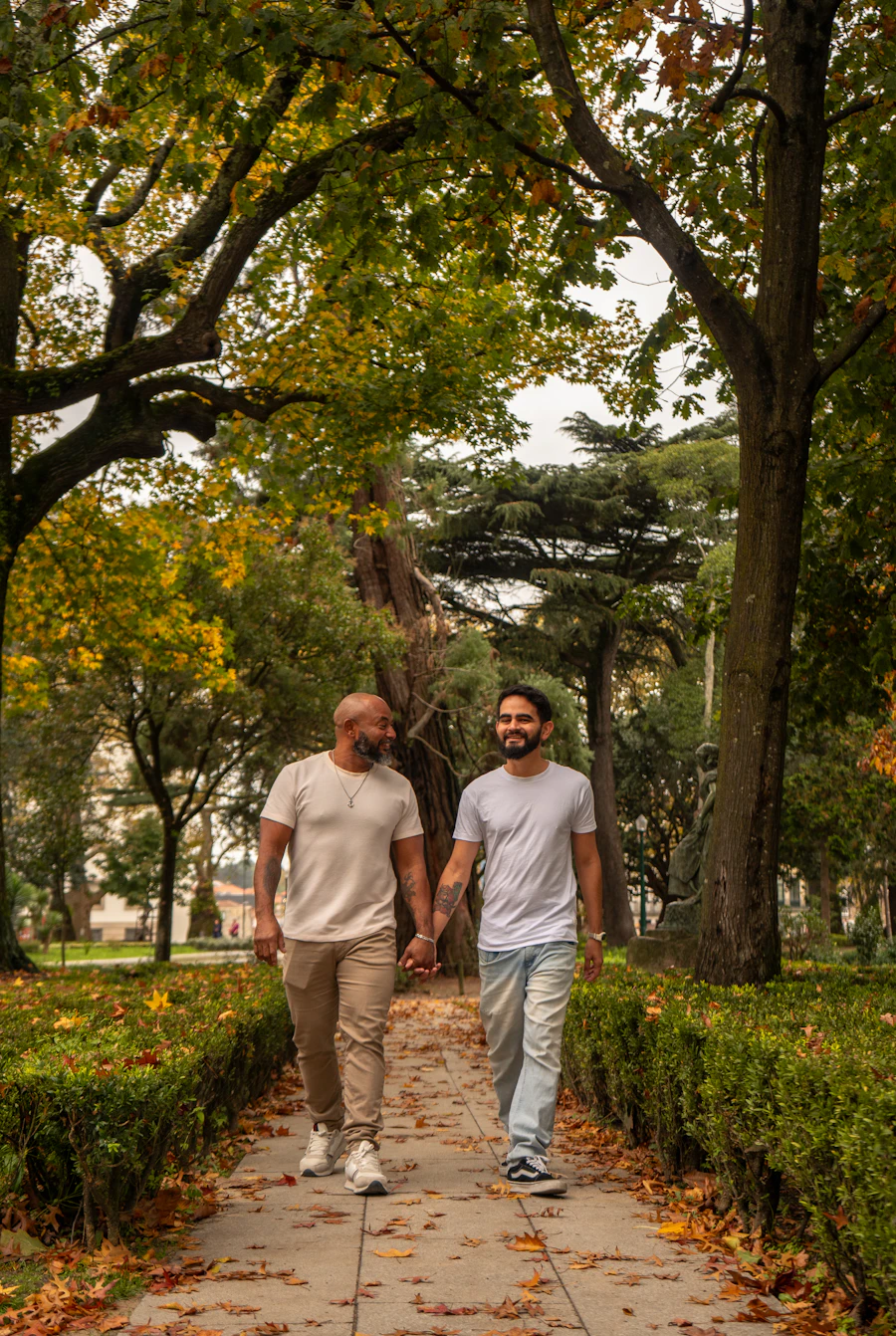 Two men walking hand in hand down a calm, tree-lined path in the open air