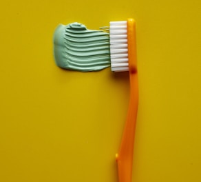 Orange toothbrush with green toothpaste on yellow background
