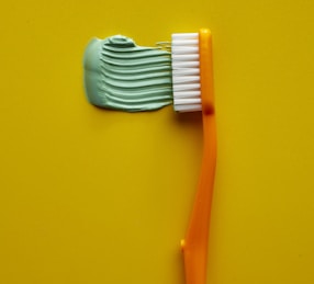 Orange toothbrush with green toothpaste on yellow background