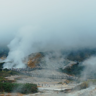 People walk on a boardwalk through steaming geothermal landscape.