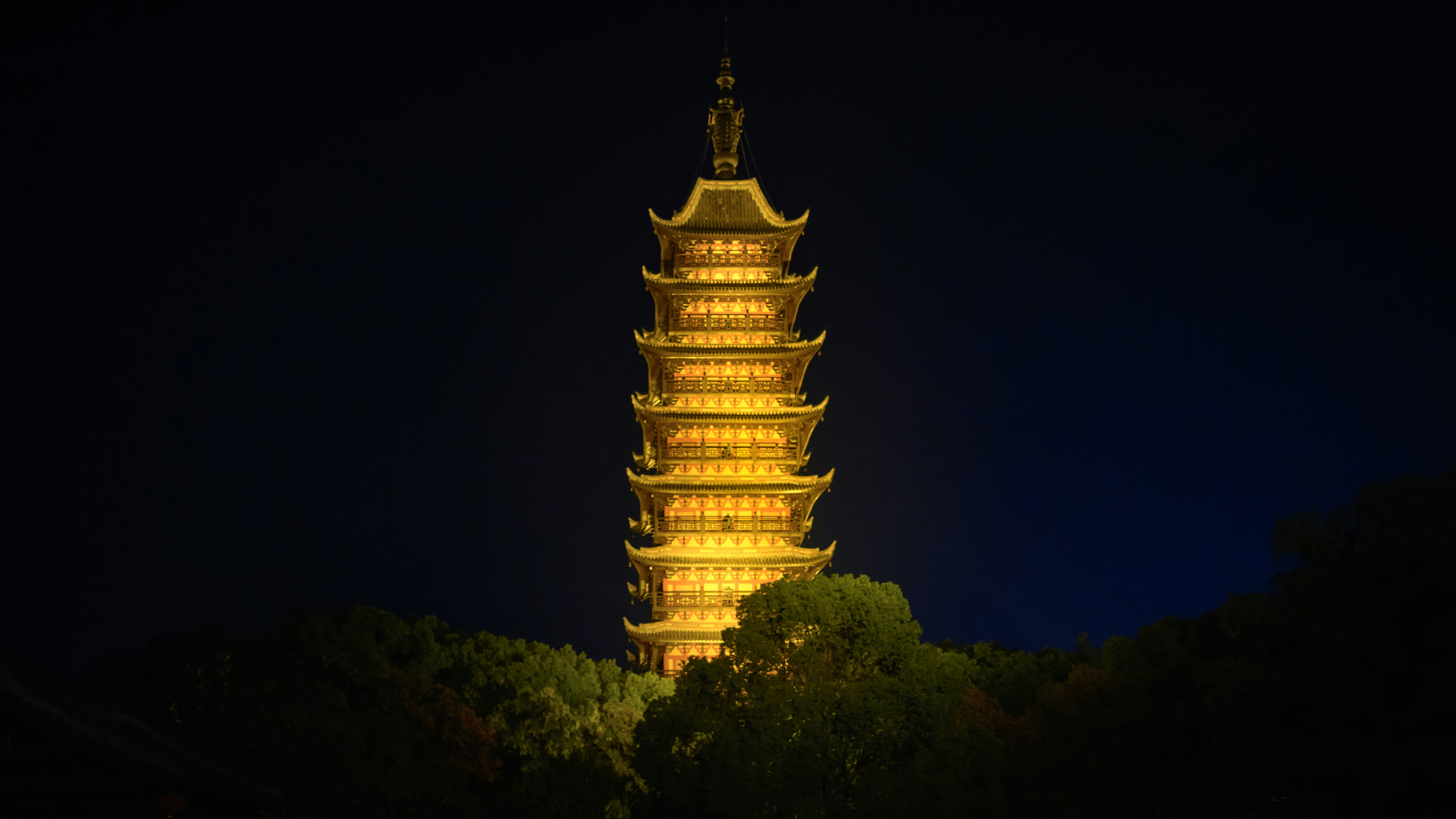 Illuminated pagoda tower at night with trees