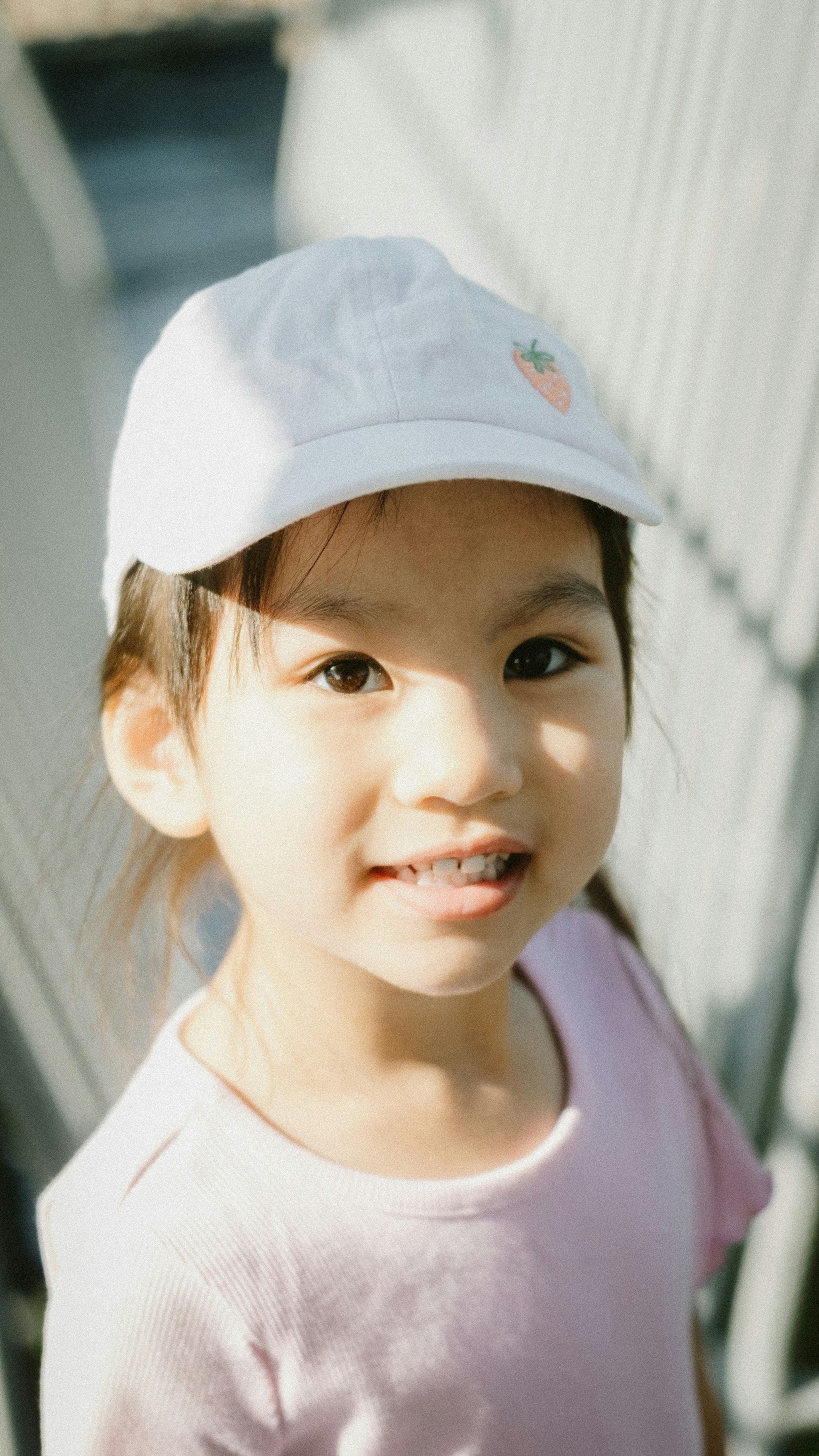 A young girl wearing a white cap and pink shirt.