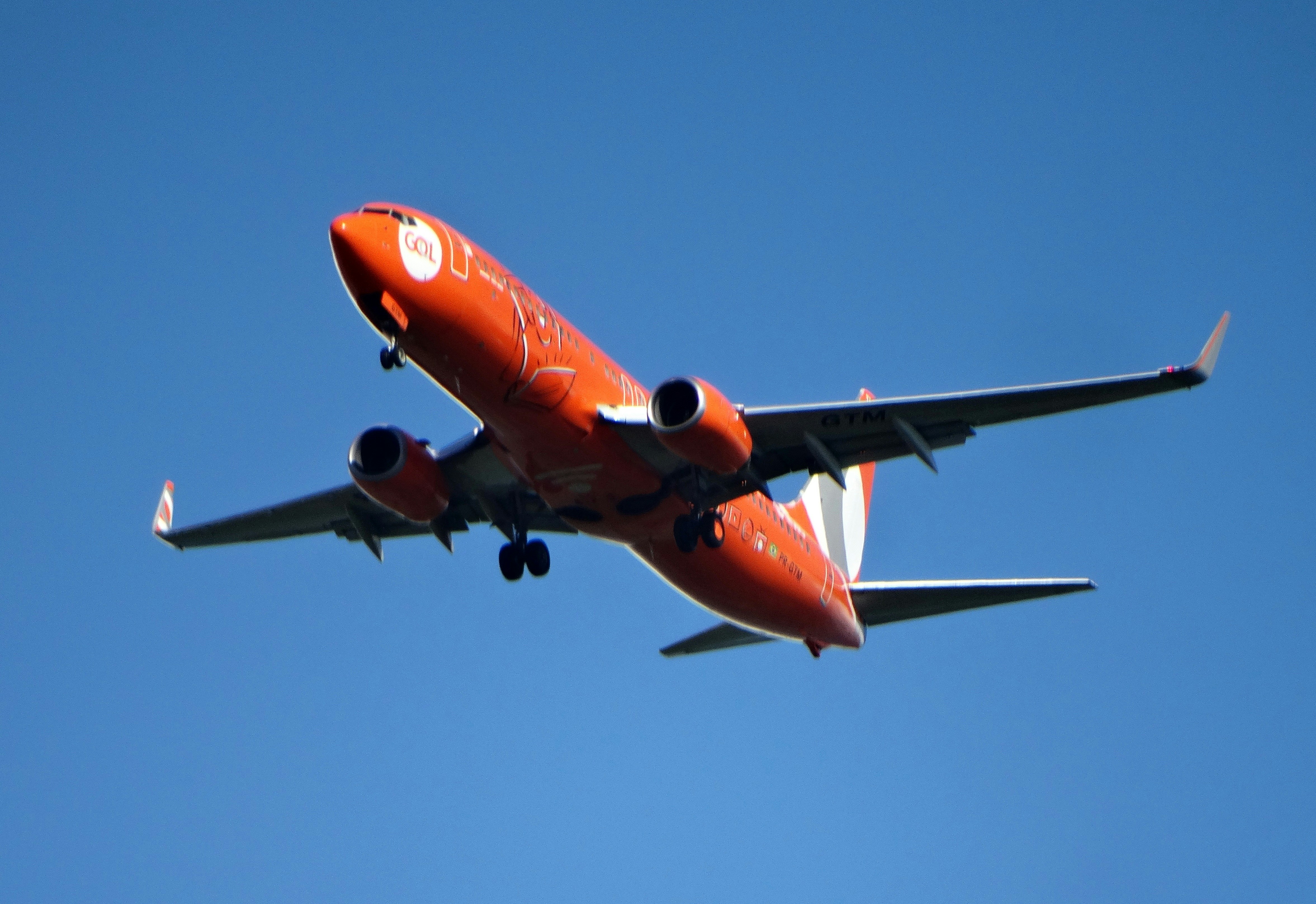 An orange airplane flying in a clear blue sky