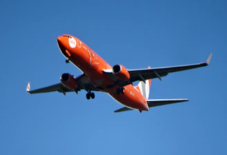 An orange airplane flying in a clear blue sky