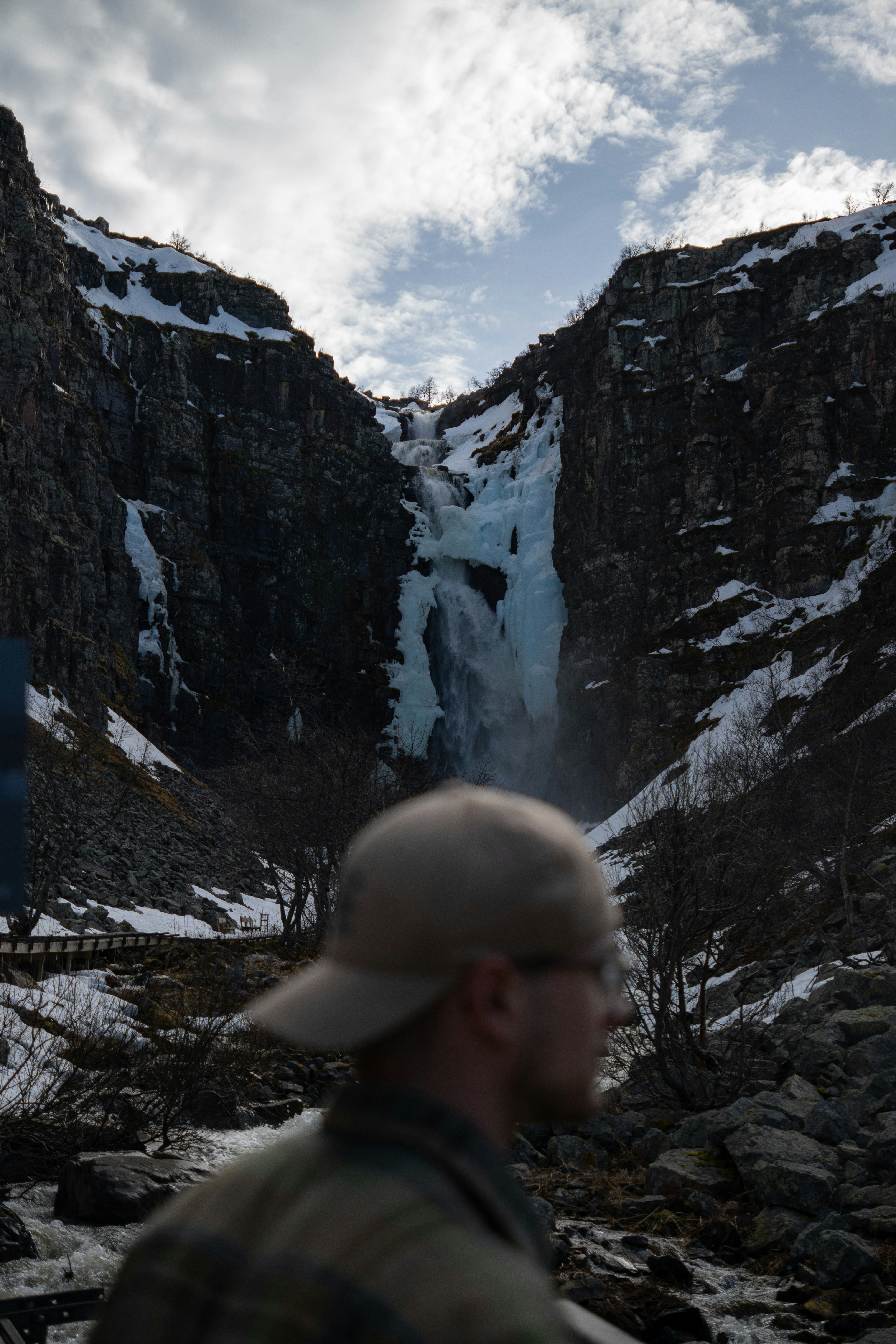 Man in cap near icy waterfall in rocky canyon