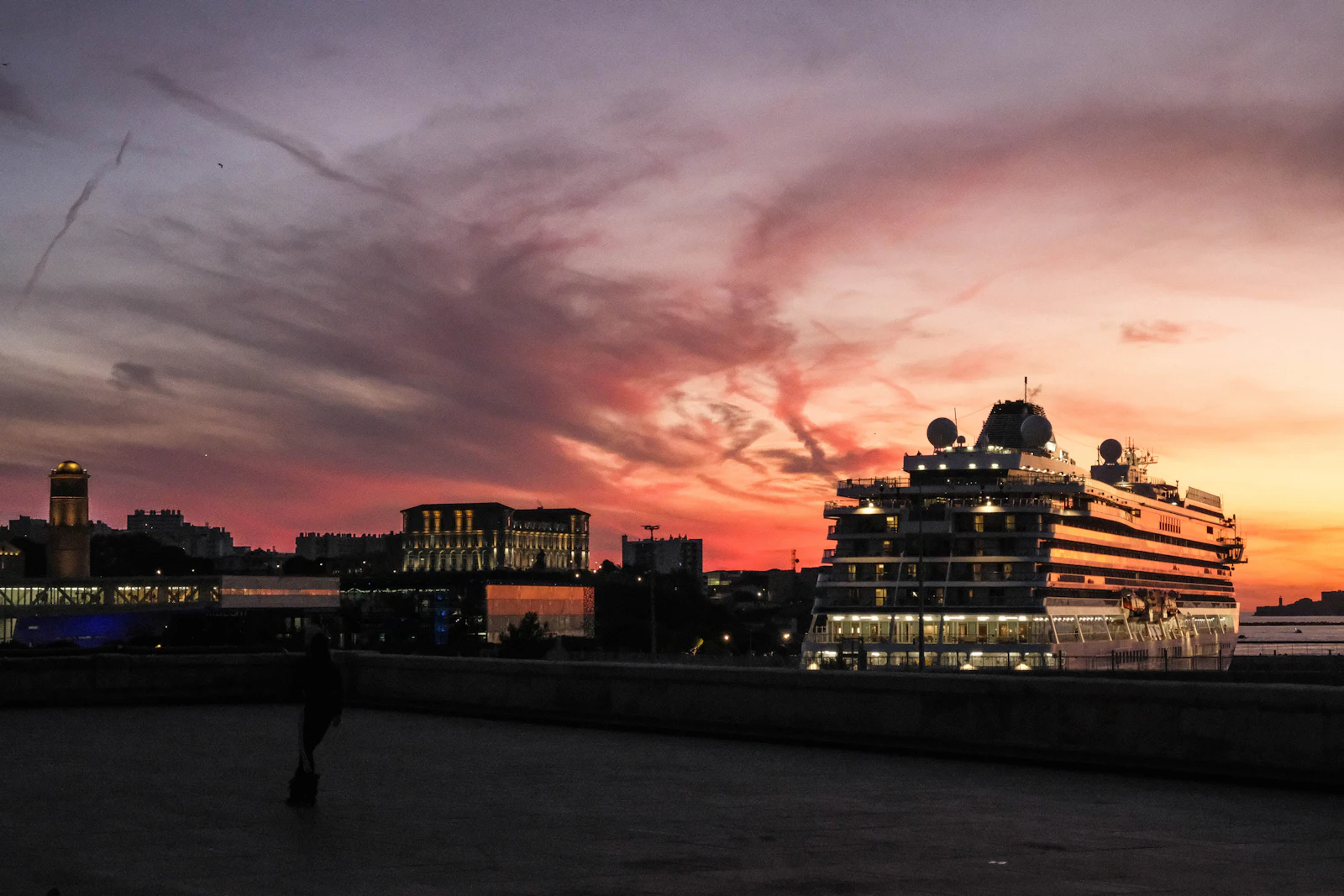 Cruise ship docked beside a European port city under a vivid pink and orange evening sky