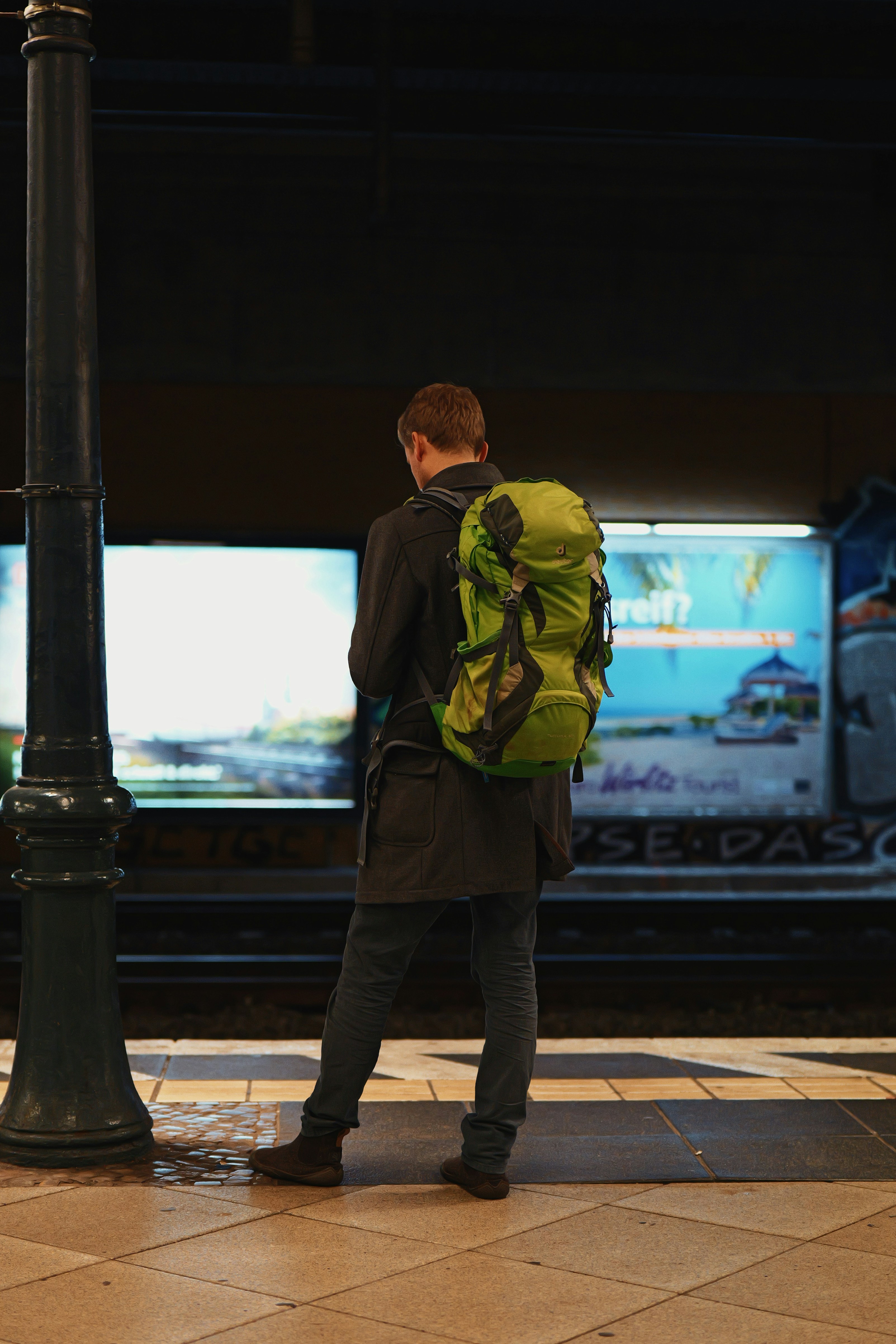 Man with green backpack waits on subway platform. - man-with-green-backpack-waits-on-subway-platform-HnZY_vAfovM