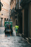 Street cleaner washing alleyway with hose from truck