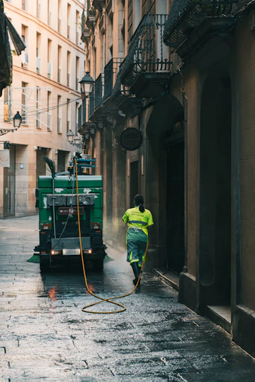 Street cleaner washing alleyway with hose from truck