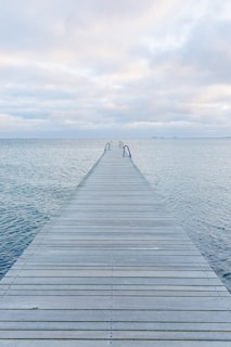 Wooden pier extending into a calm, overcast ocean.