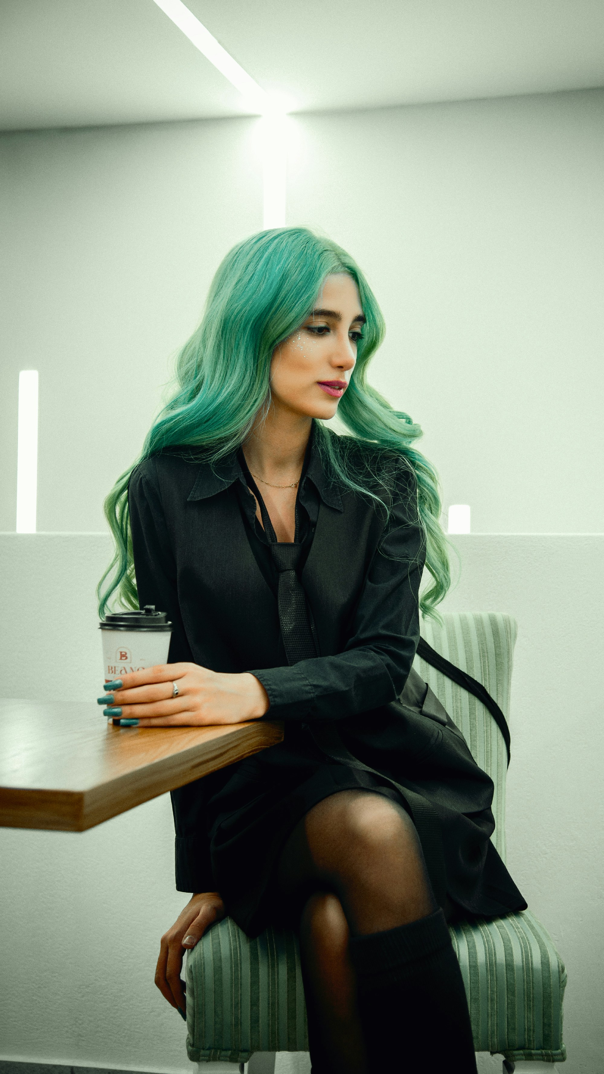 Woman with teal hair holding a coffee cup at table.