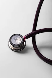 A close-up of a burgundy stethoscope on a white surface.