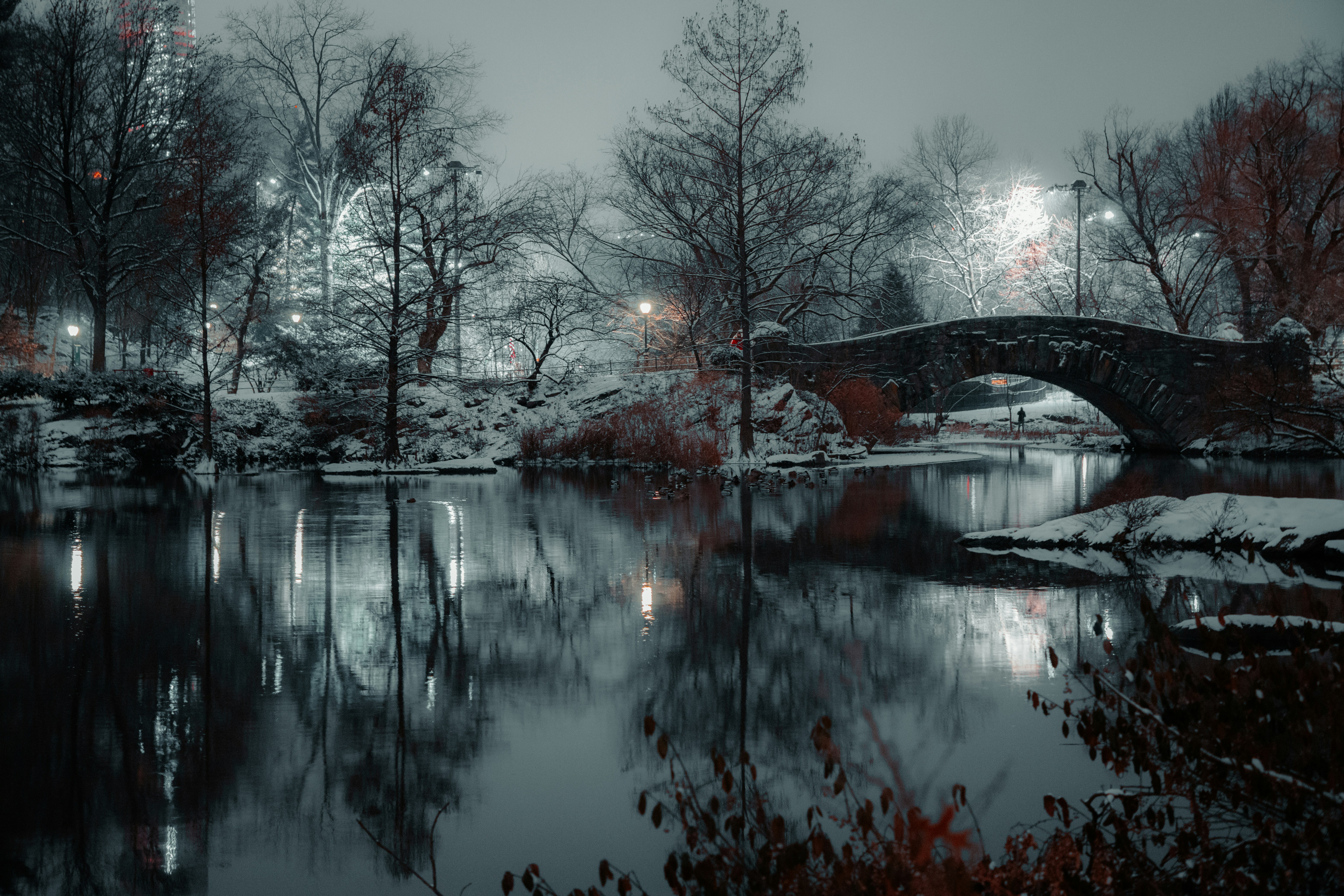 Verschneiter Park mit Steinbrücke und Wasserreflexionen