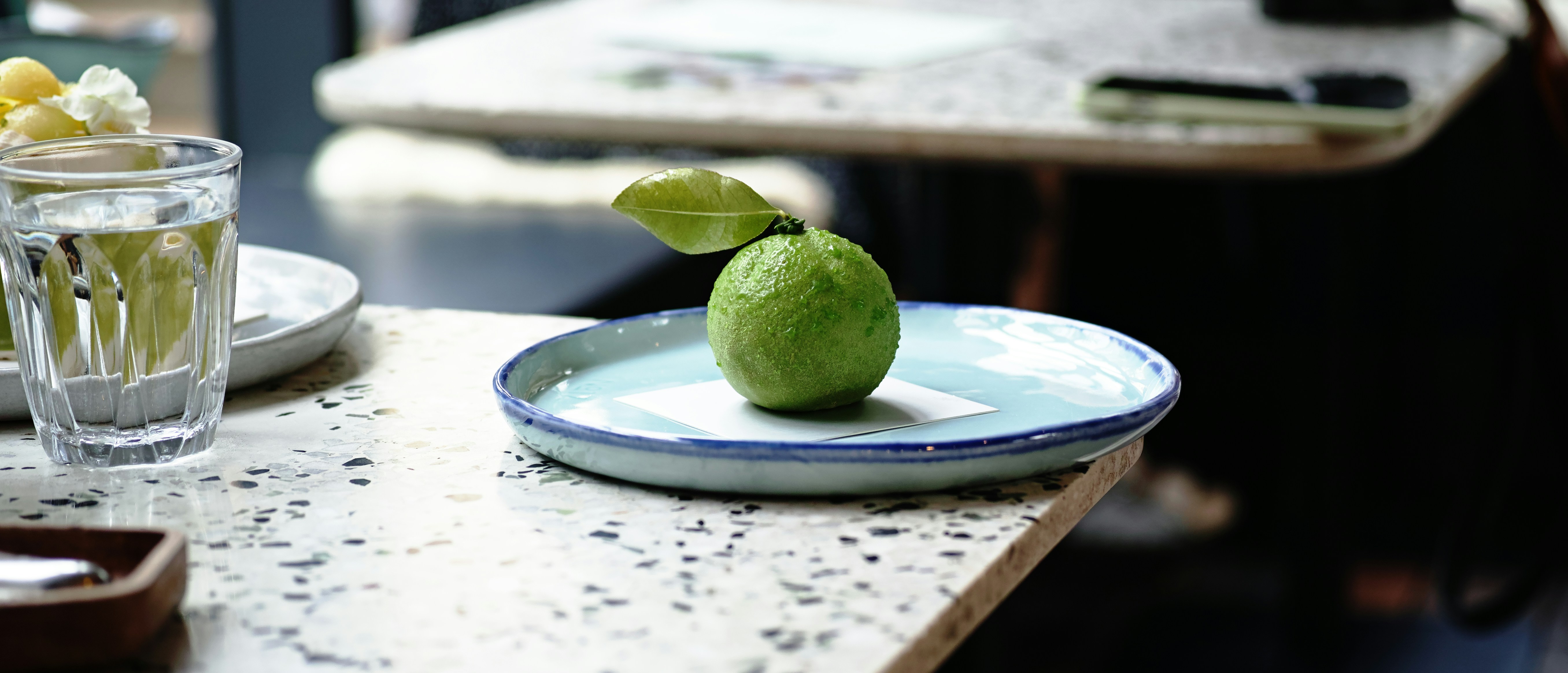 A single green lime with a leaf on a plate.