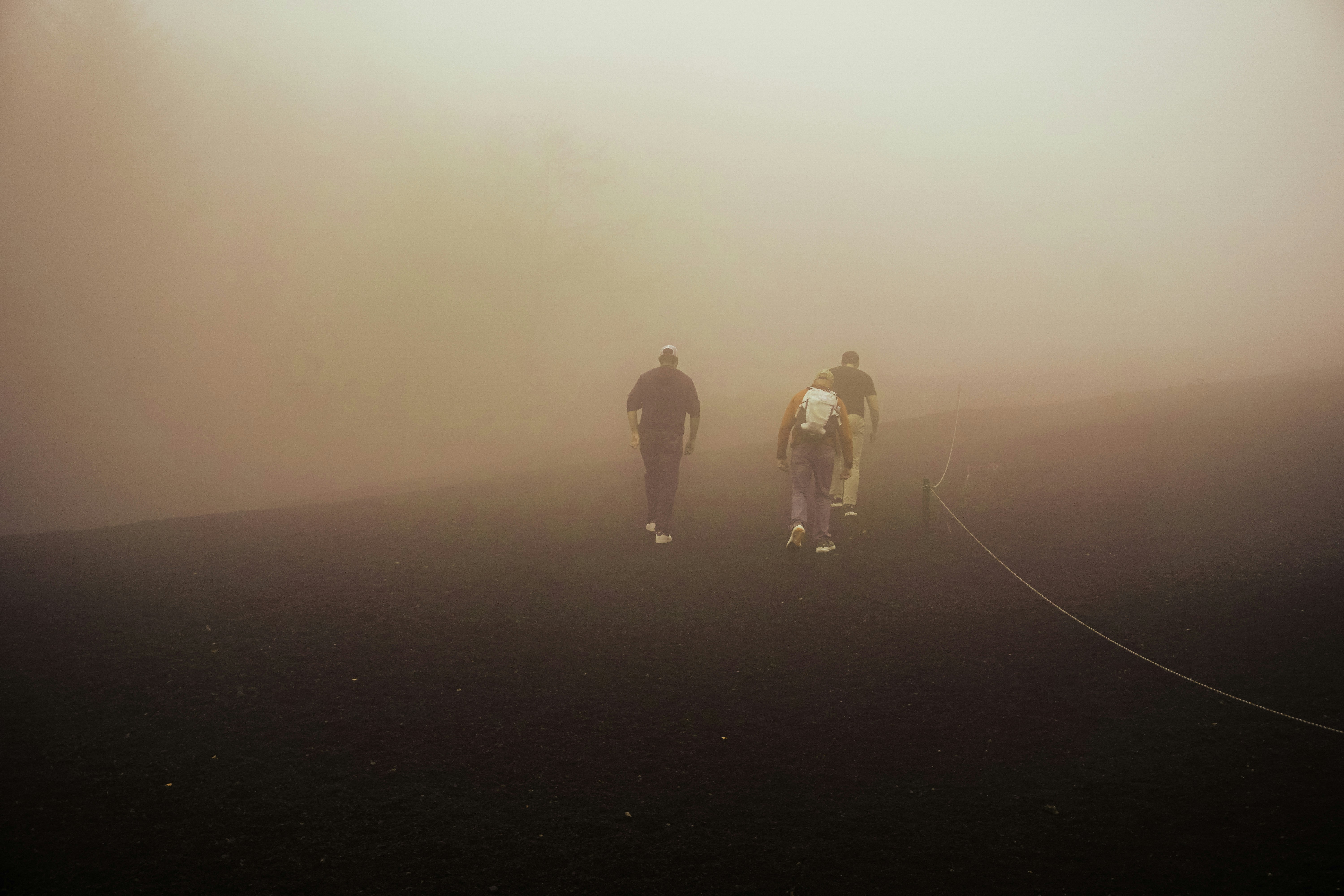 Three people walk on a path through fog.