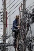 Man climbs utility pole with many tangled wires