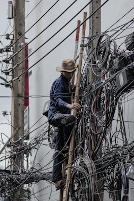 Man climbs utility pole with many tangled wires