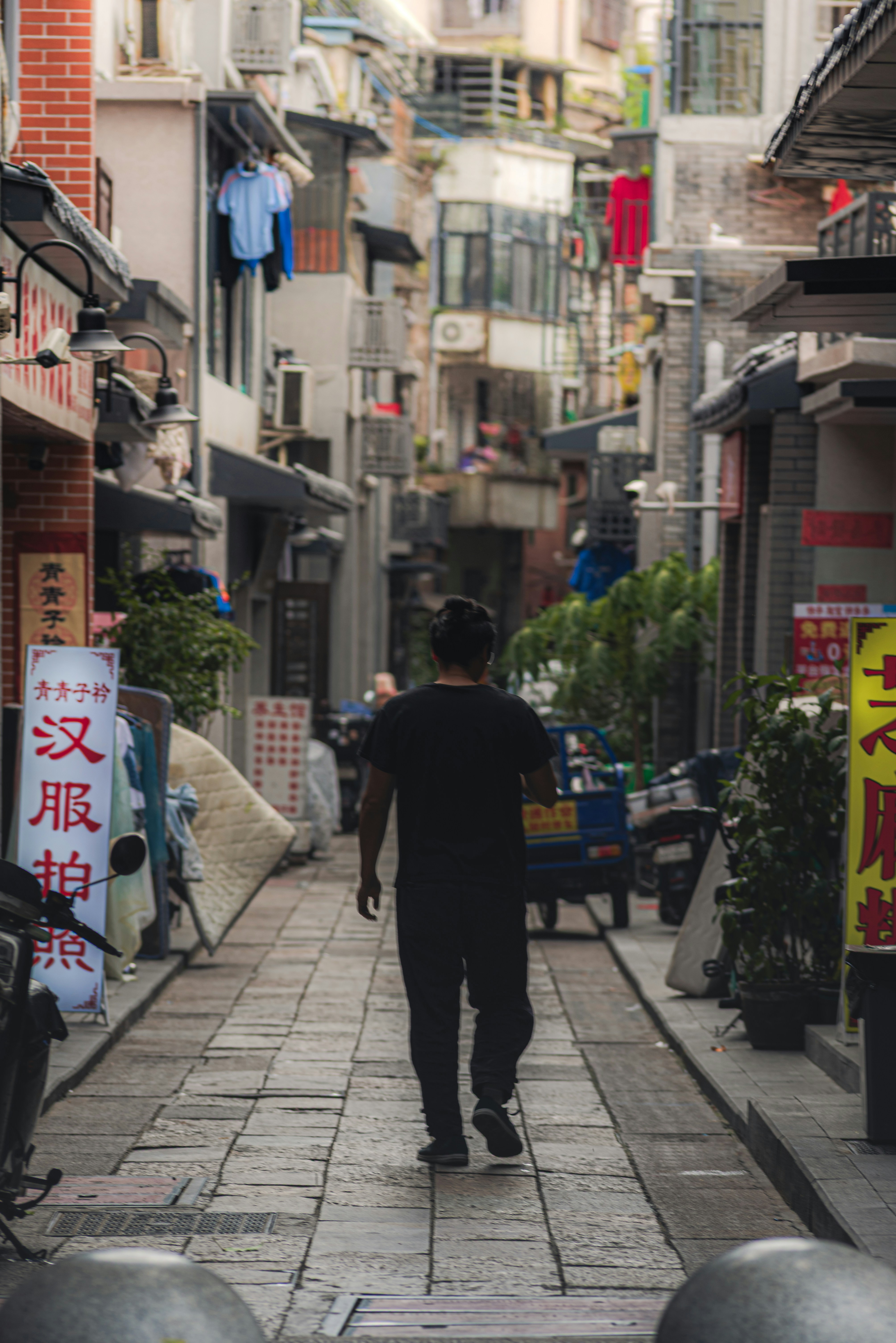 Man walks down a narrow street with buildings.
