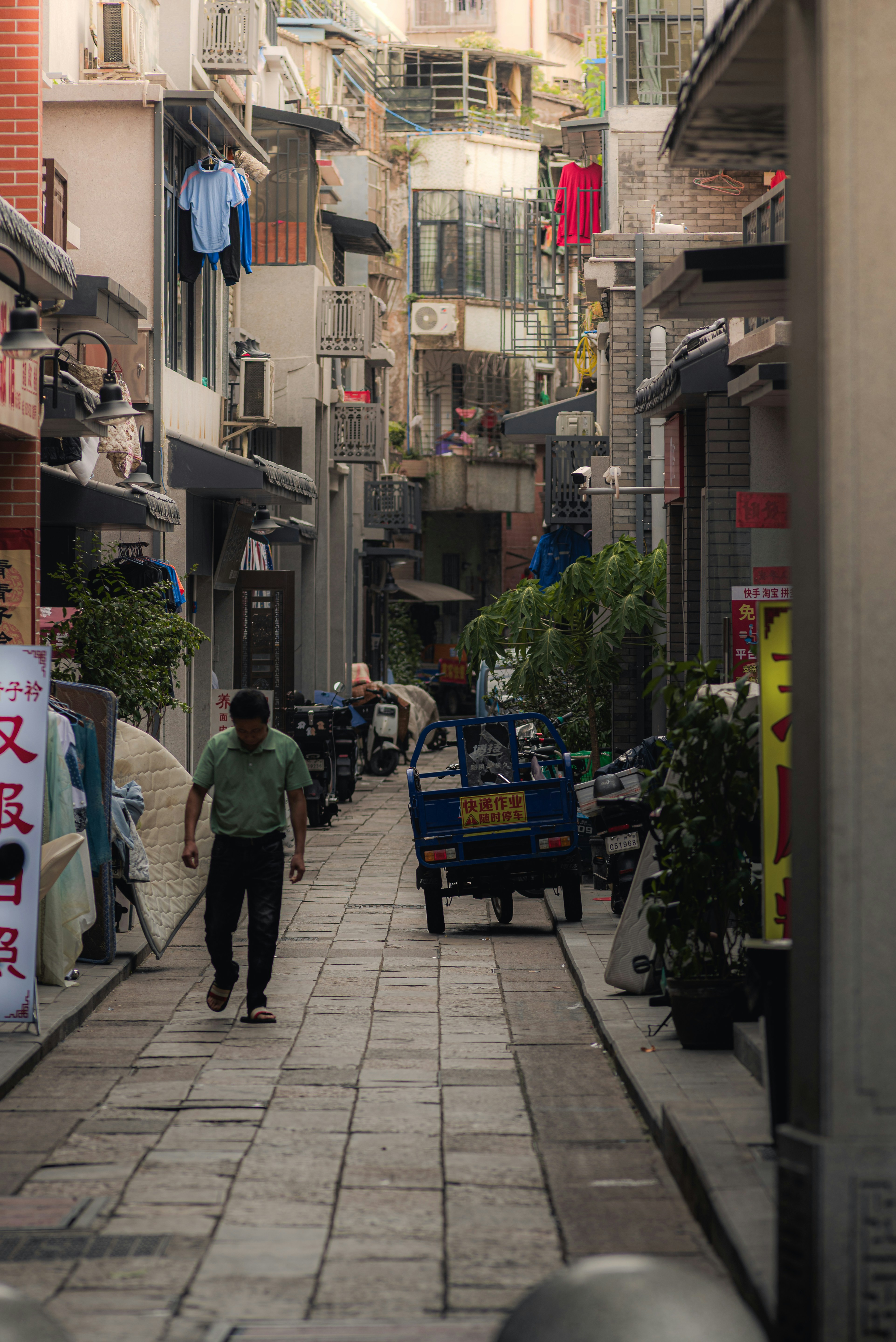 Man walks down a narrow street with buildings and scooters.