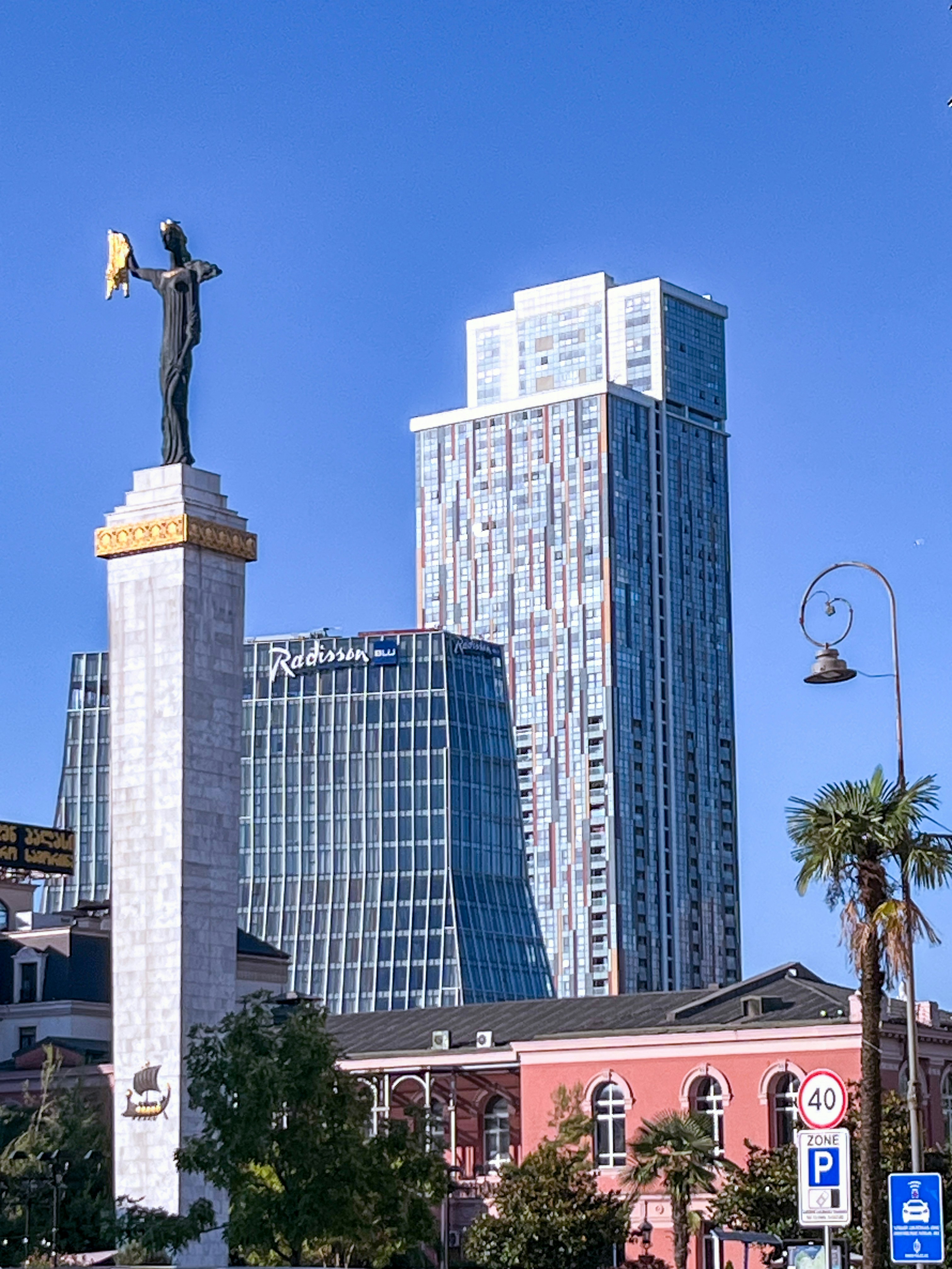 Statue and modern buildings against a blue sky.