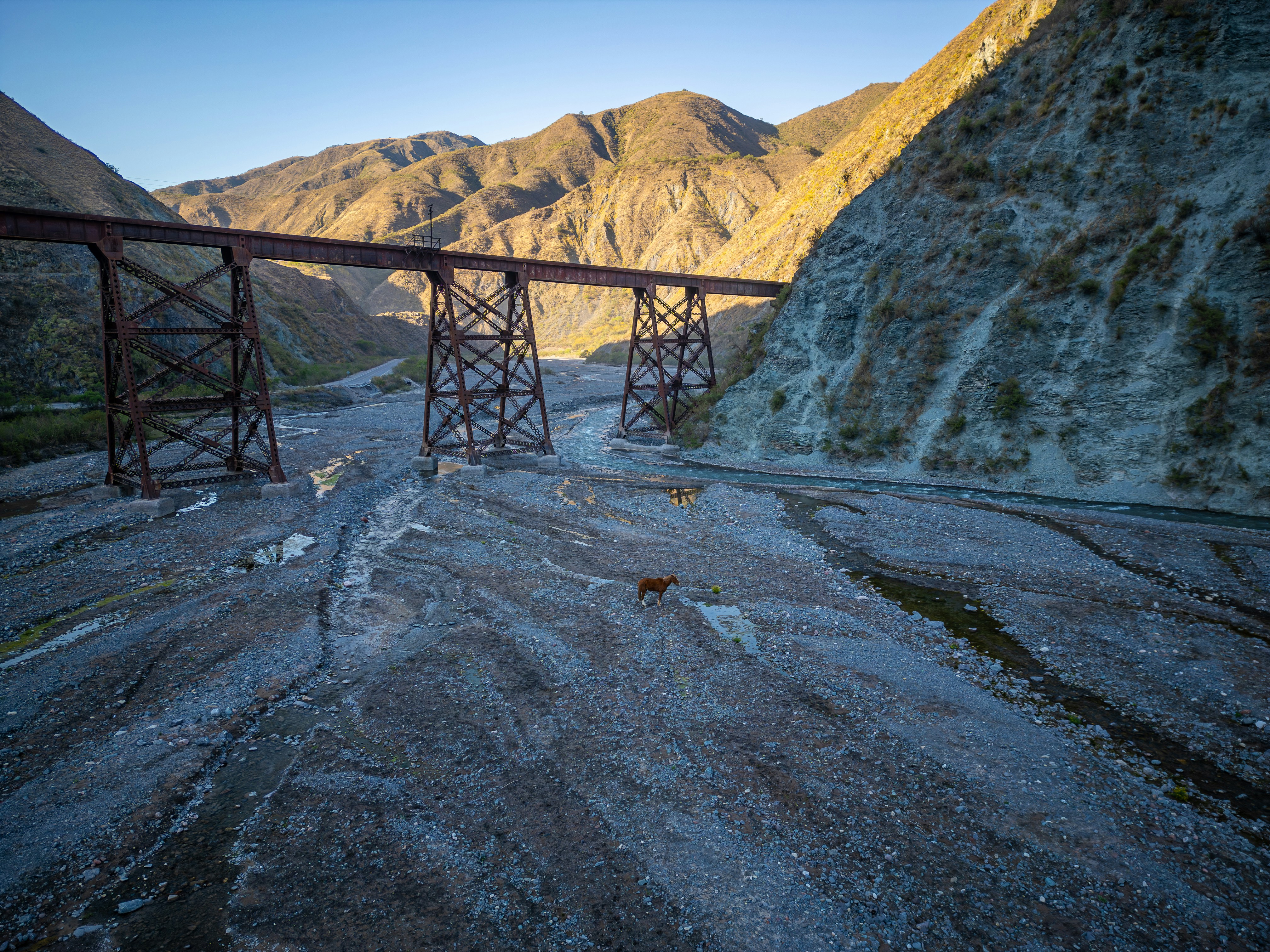 Old railway bridge over a dry riverbed with mountains.