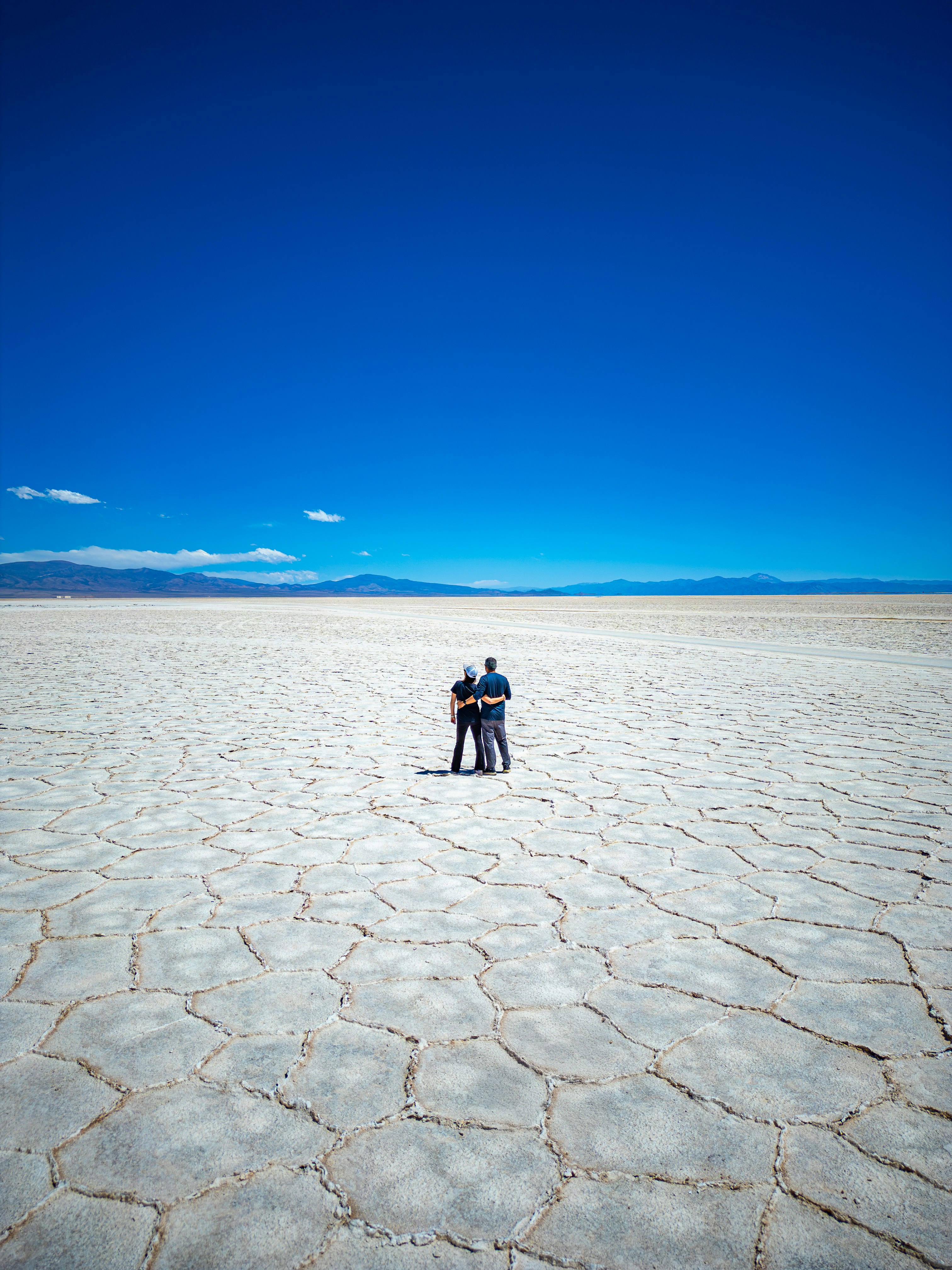 Coppia in piedi su vasto piatto di sale crepato sotto il cielo blu