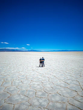 Couple standing on vast cracked salt flat under blue sky