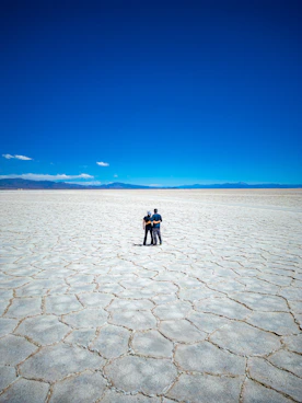 Couple standing on vast cracked salt flat under blue sky