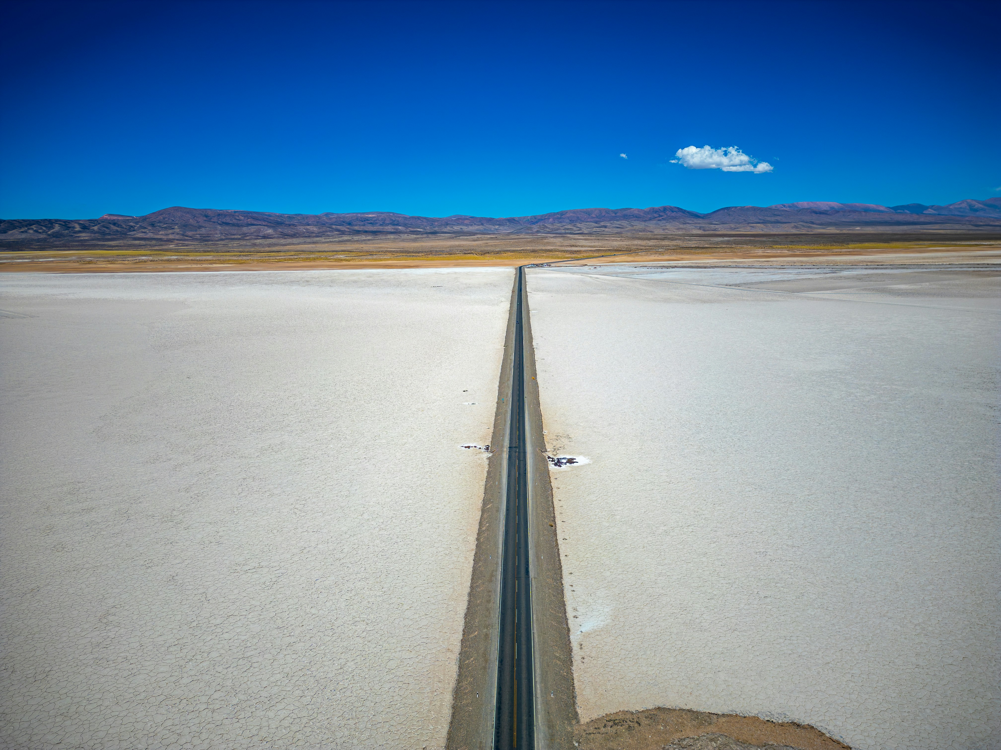 Long straight road through a vast white desert.