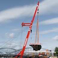 Red crane lifting a boat hull over water
