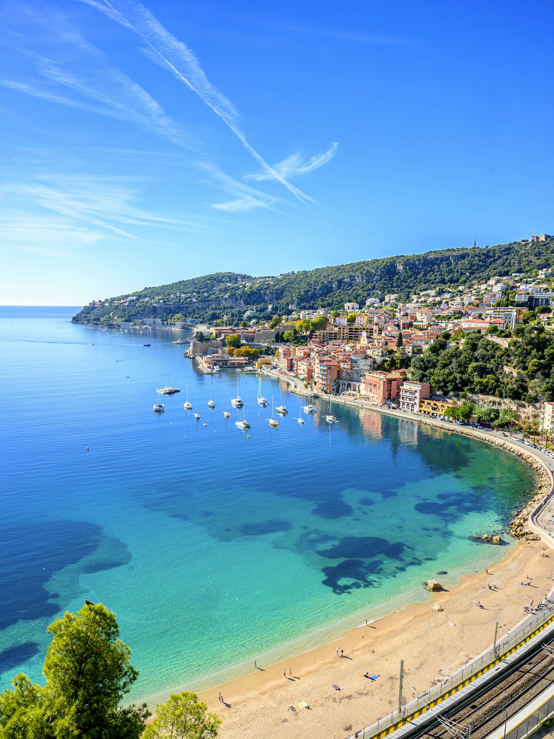 Coastal town with boats in turquoise water and beach.