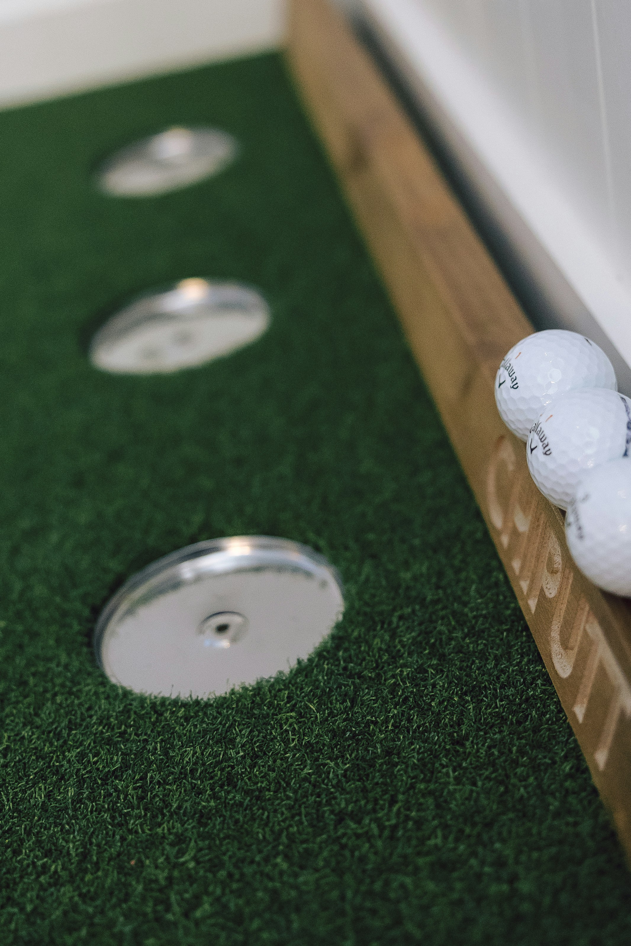 Golf balls rest on a chipping green next to holes.