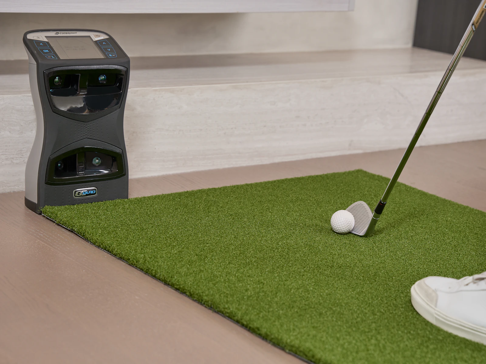 Launch monitor placed behind a golf ball on an indoor mat