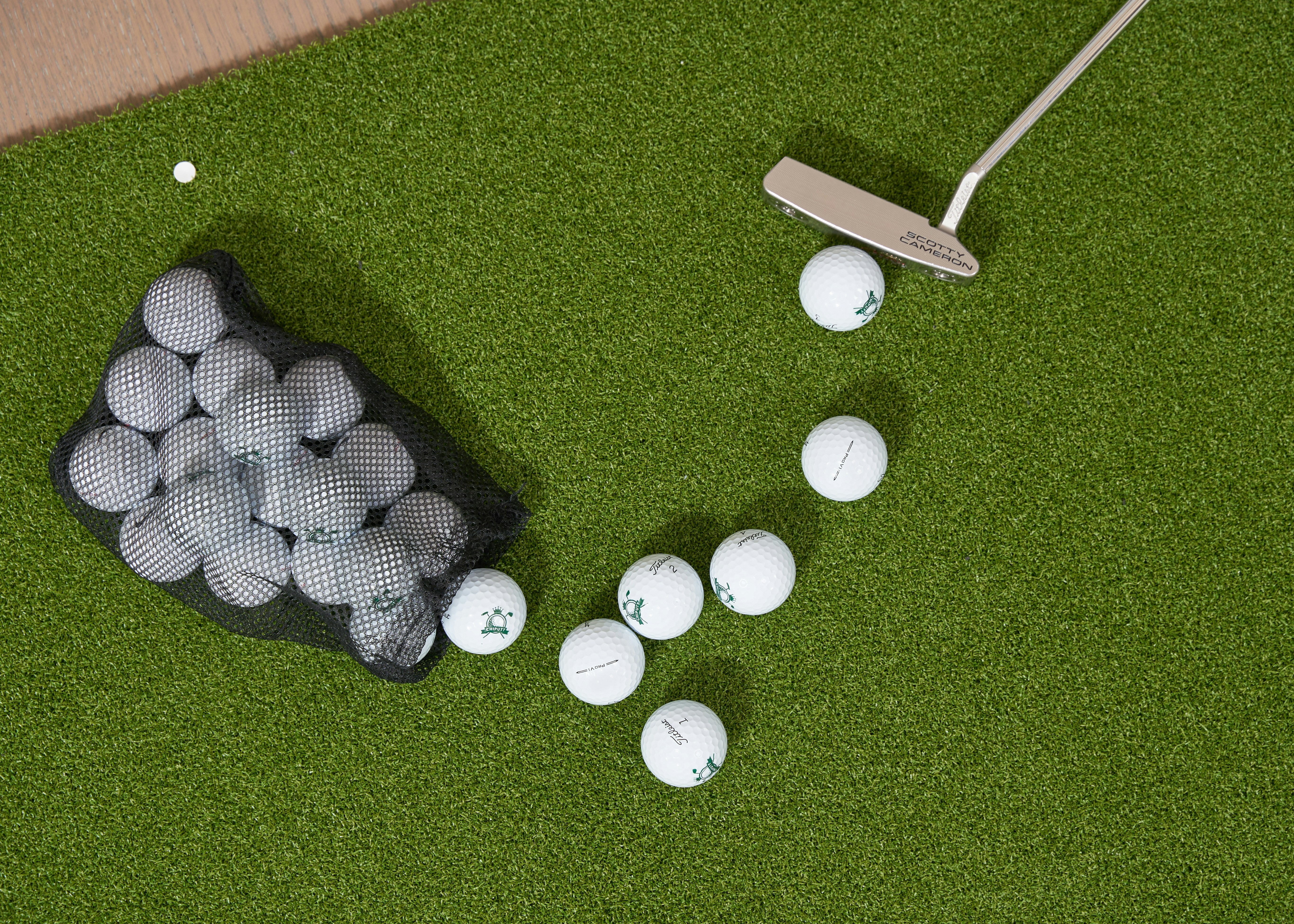 Image by Chiputt Golf. Learn more at TheChiputt.com. A top-down view of an indoor practice green scattered with golf balls beside a mesh bag and a putter. The textured turf, simple composition, and natural lighting create a calm, focused scene that captures the quiet routine of home putting practice.